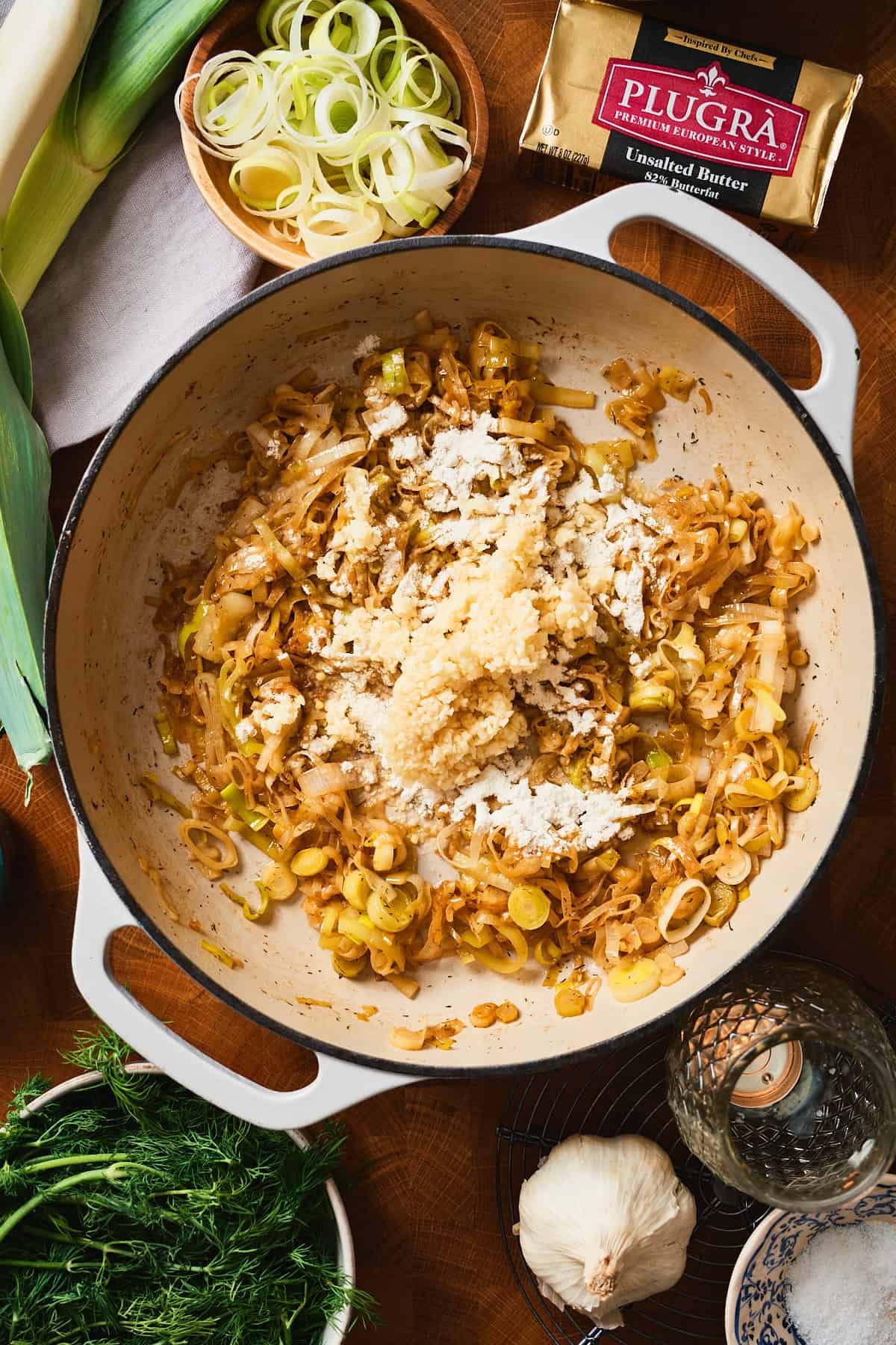 Flour and minced garlic added to caramelized leeks in a pan.