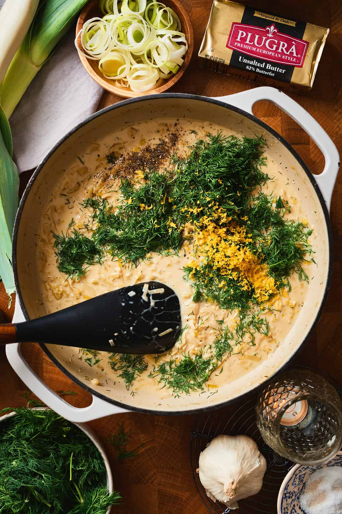 Fresh dill and lemon zest added to a creamy leek sauce in a pan.
