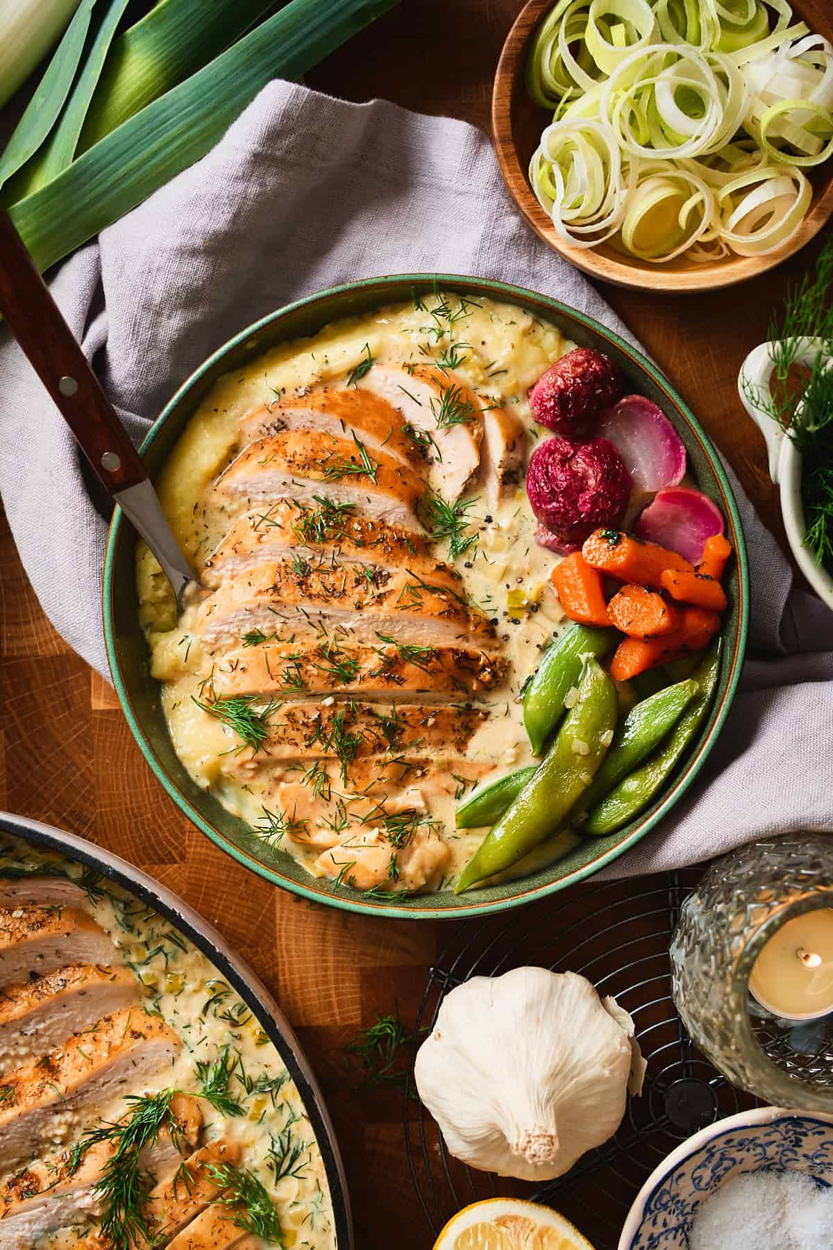 Bowl of sliced chicken in lemon dill cream sauce over mashed potatoes, served with sugar snap peas, glazed carrots, and roasted radishes.