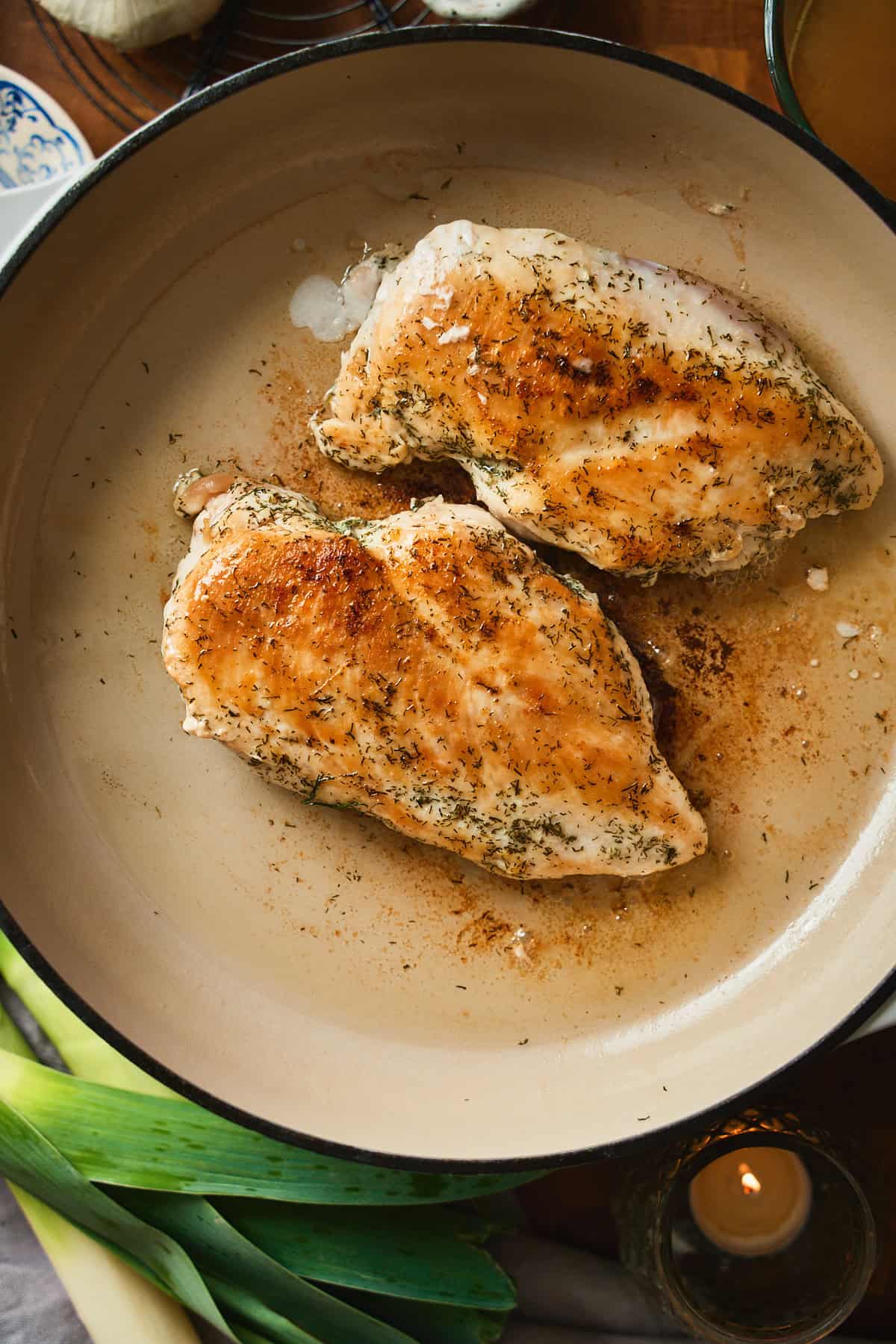 Two chicken breasts searing in a white enameled pan with a deep golden crust.