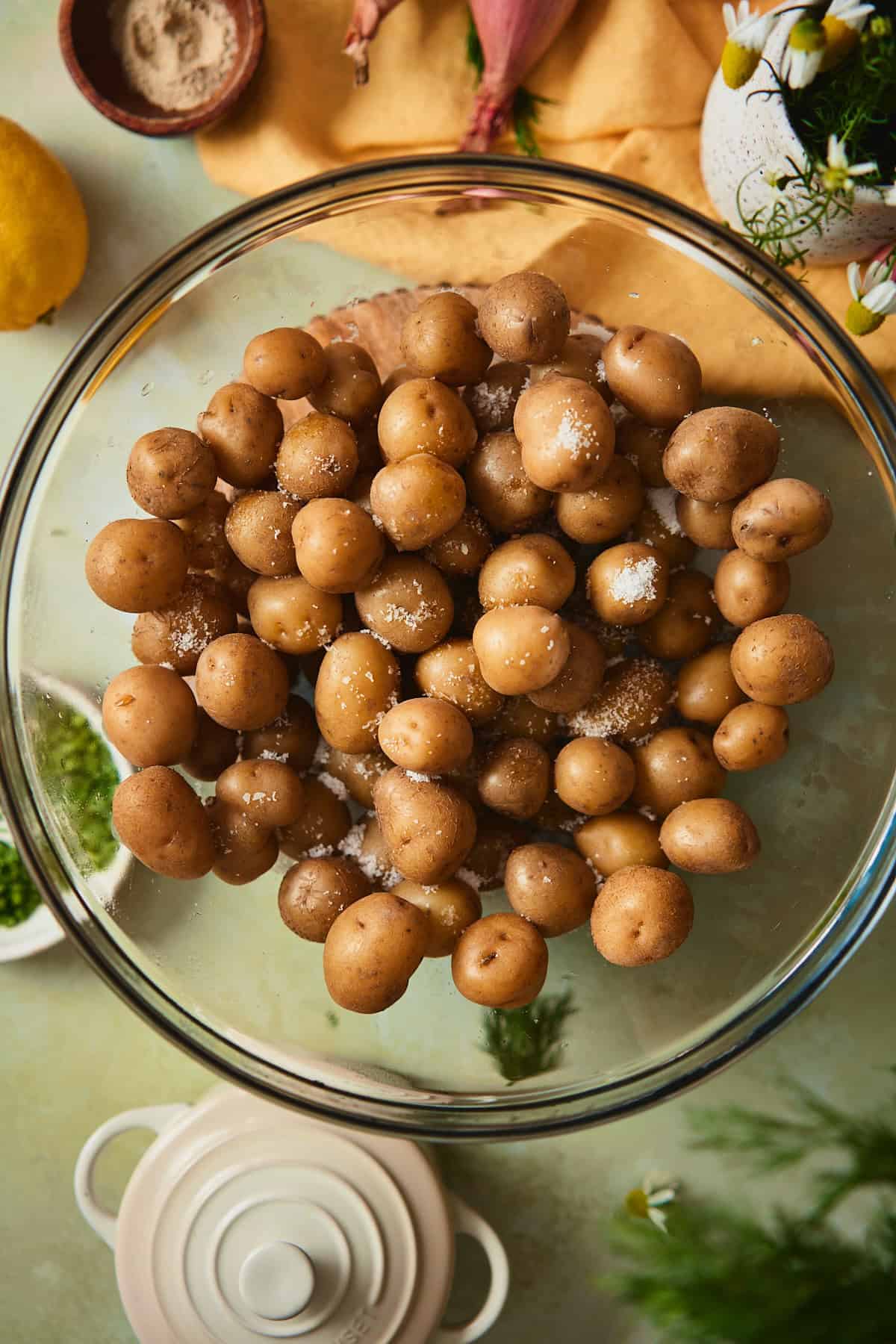 Drained baby yellow potatoes in a glass bowl with kosher salt scattered on top.