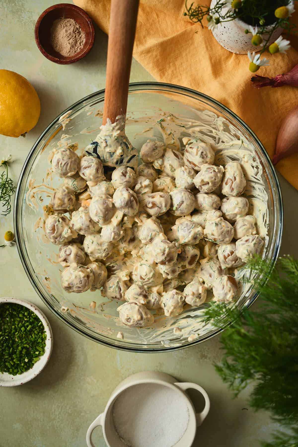 Boiled baby yellow potatoes folded into creamy dill dressing in a large glass mixing bowl.
