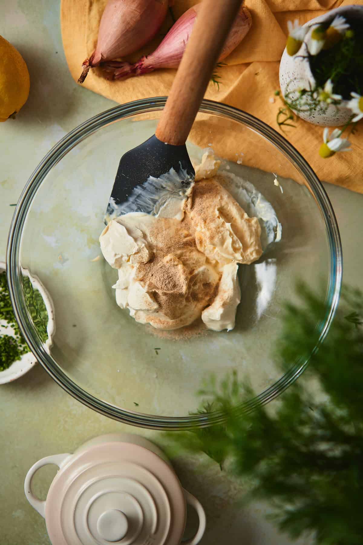 Sour cream, mayo, and white pepper in a glass mixing bowl with a spatula, ready to be whisked together.
