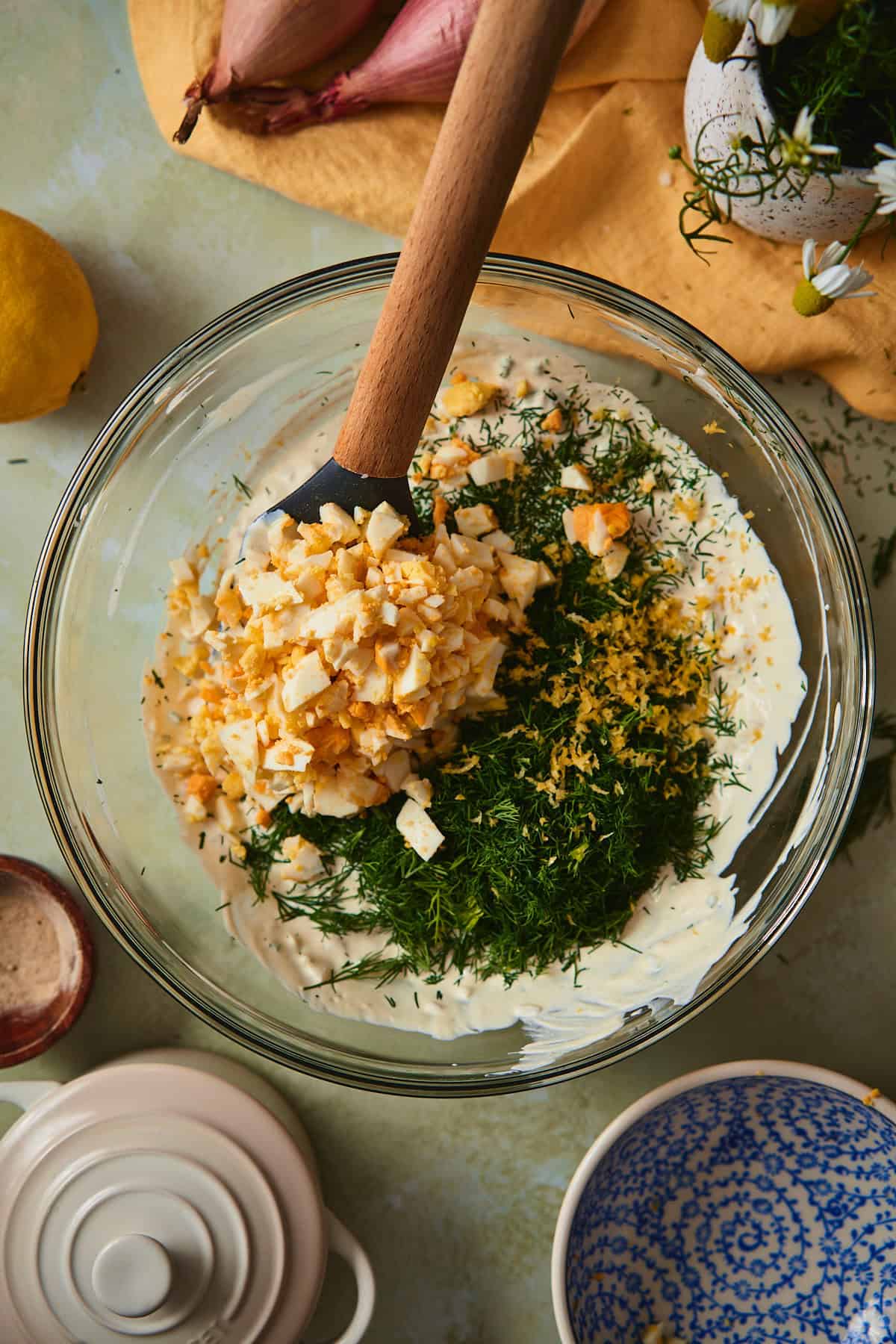 Diced hard-boiled eggs and freshly chopped dill piled on creamy dressing in a glass bowl, ready to be folded together.