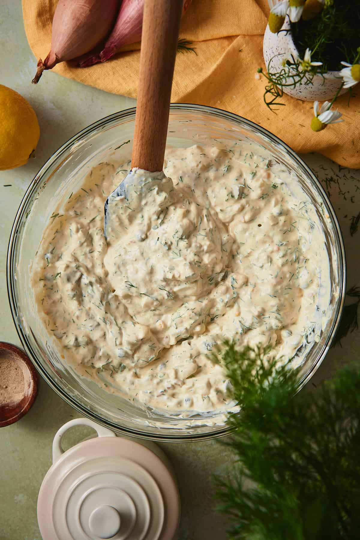 Finished sour cream dill dressing in a glass bowl, flecked with fresh dill, chives, and tiny pieces of pickles and shallot.