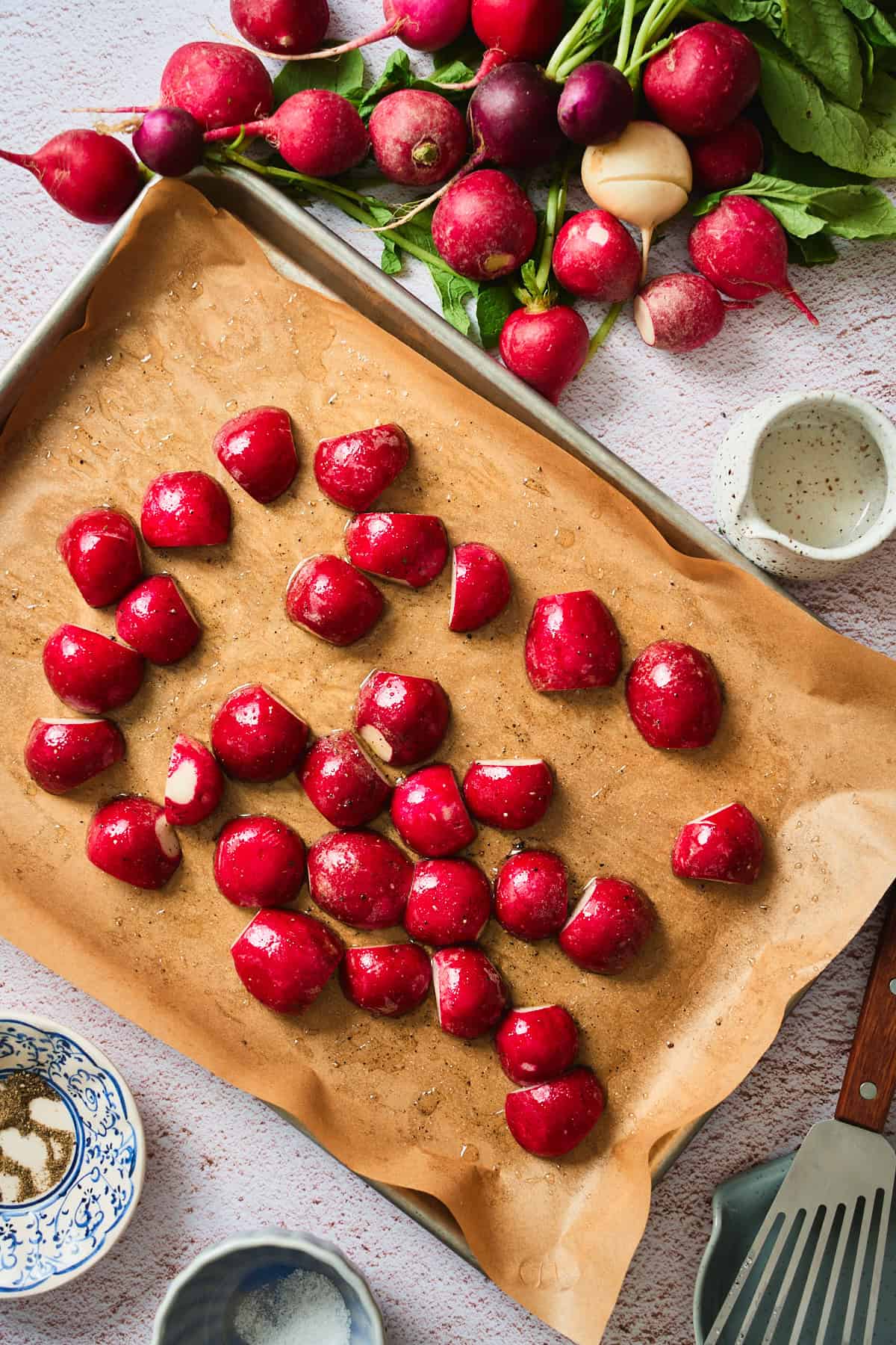 Seasoned raw radishes cut-side-down on parchment, sprinkled with kosher salt and black pepper.