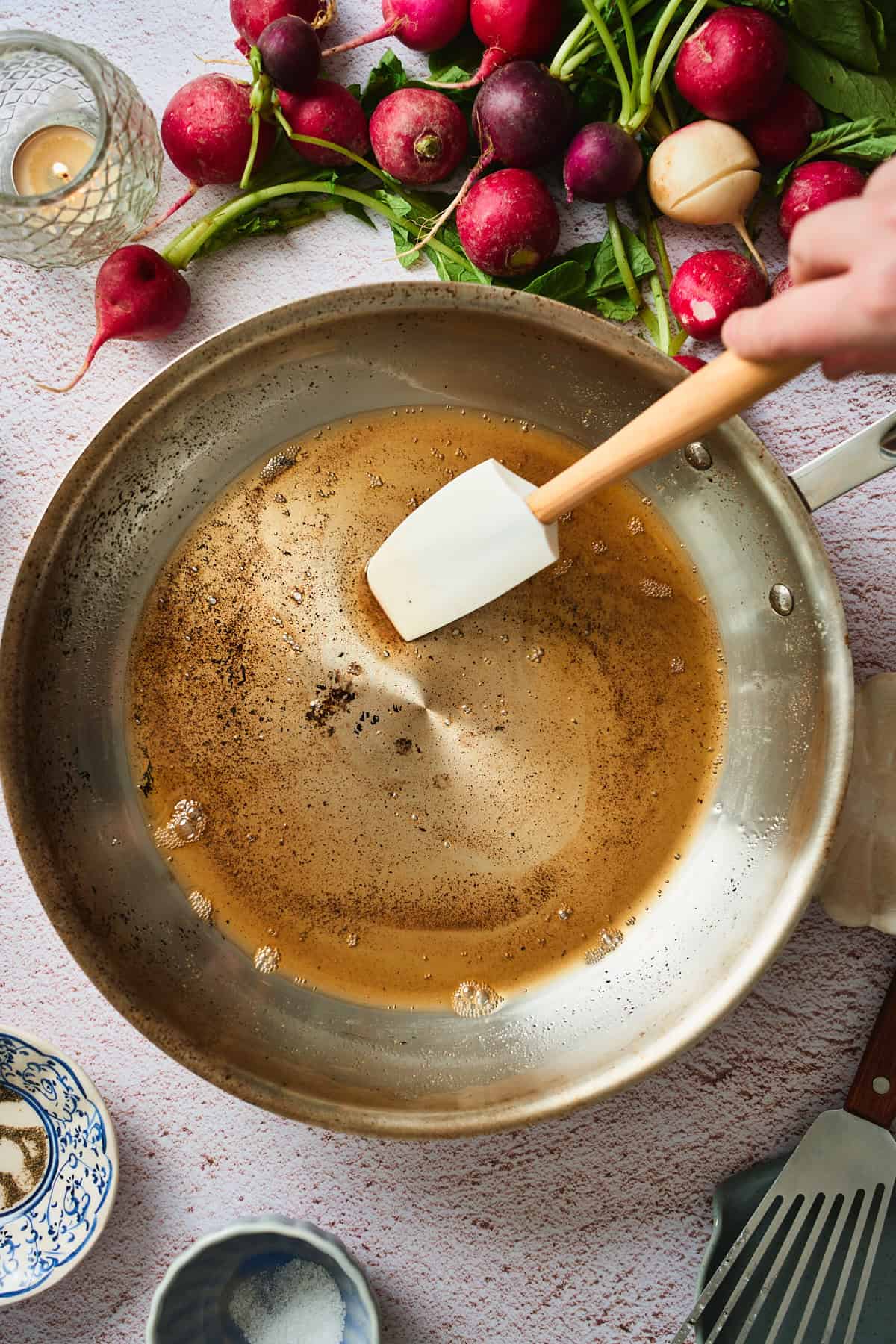 Hand swirling deeply browned butter in a stainless skillet with a spatula.