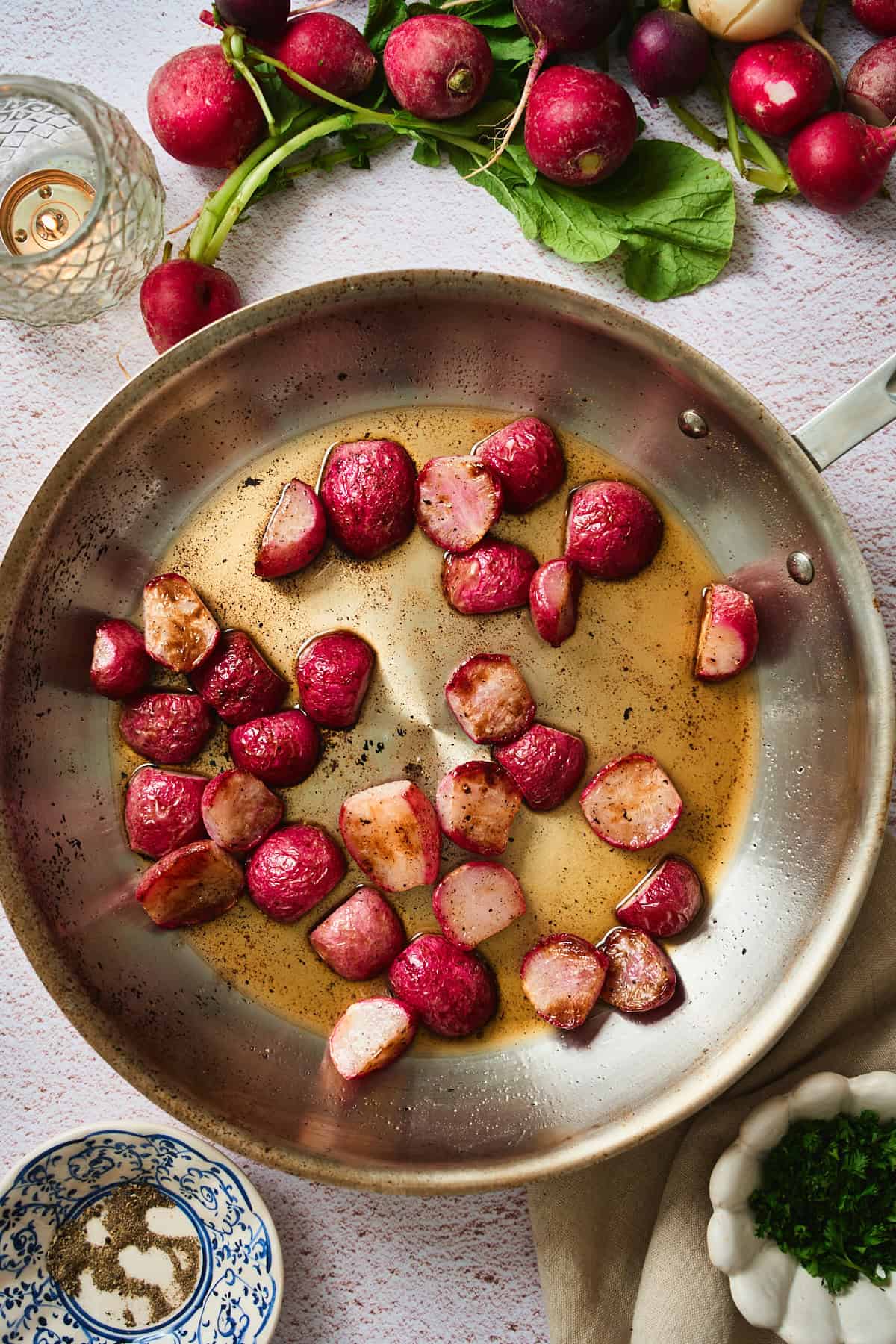 Roasted radishes being tossed in brown butter in a skillet with a metal spatula.