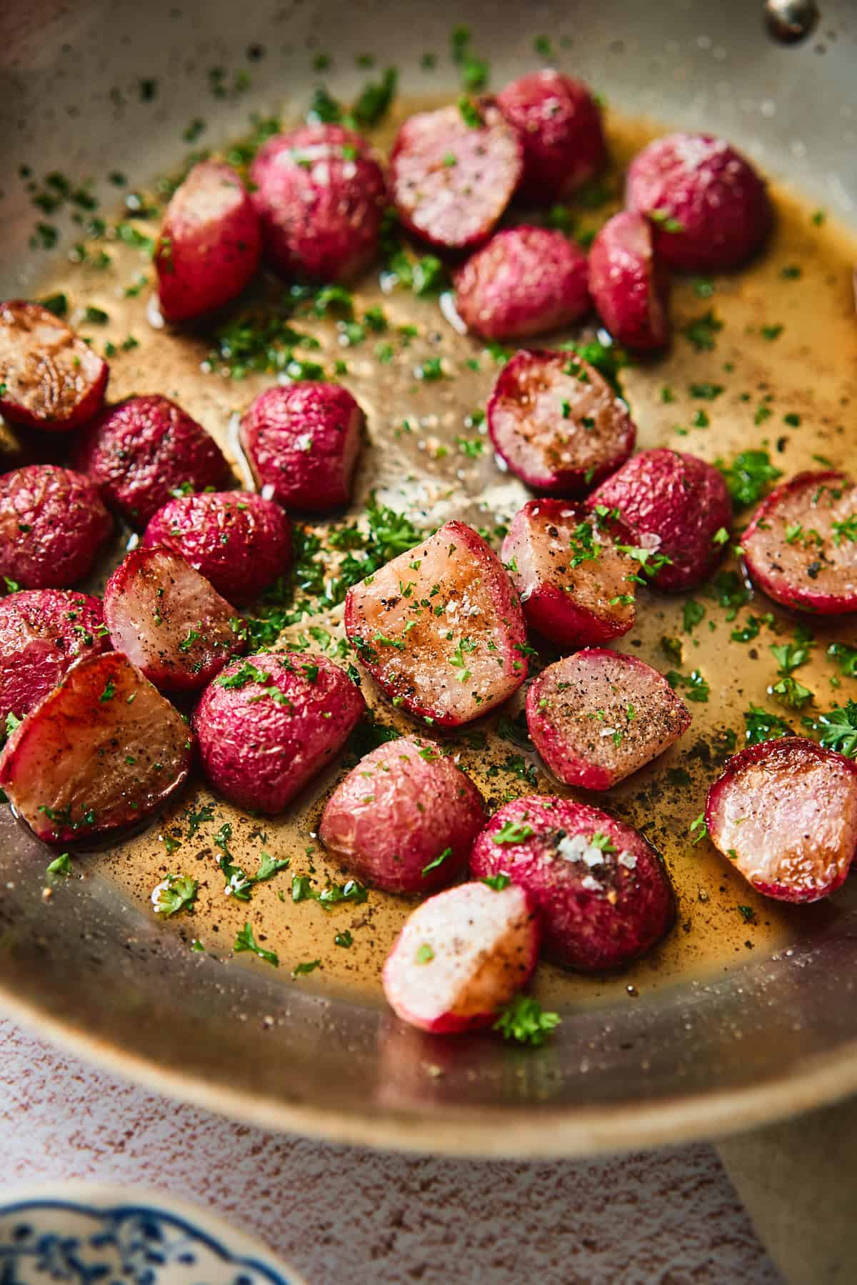 Close-up of roasted radishes glistening in brown butter with fresh parsley and flaky salt.