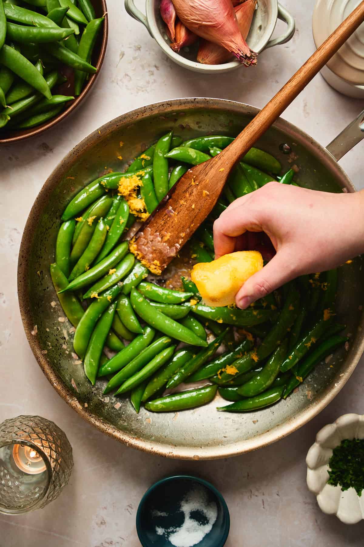 Hand squeezing lemon juice over sautéed snap peas in a skillet.