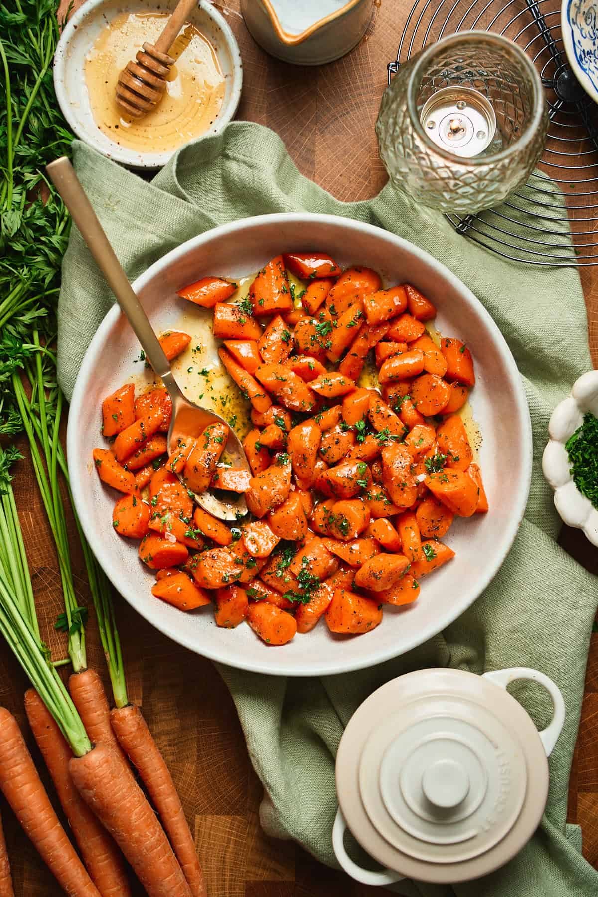 Overhead of honey butter glazed carrots in a serving bowl with serving spoons, whole carrots alongside.