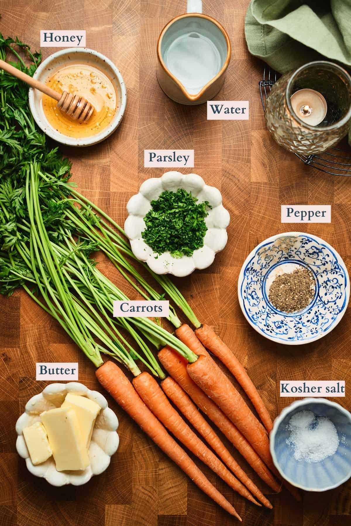 Ingredients for stovetop glazed carrots labeled on a flat lay: carrots, butter, honey, water, kosher salt, parsley, and pepper.