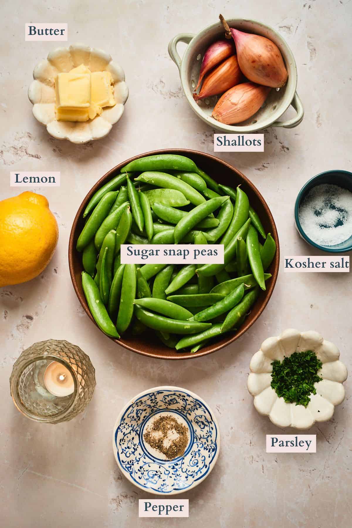 Ingredients for sautéed sugar snap peas laid out and labeled - snap peas, butter, shallots, lemon, parsley, salt, and pepper.