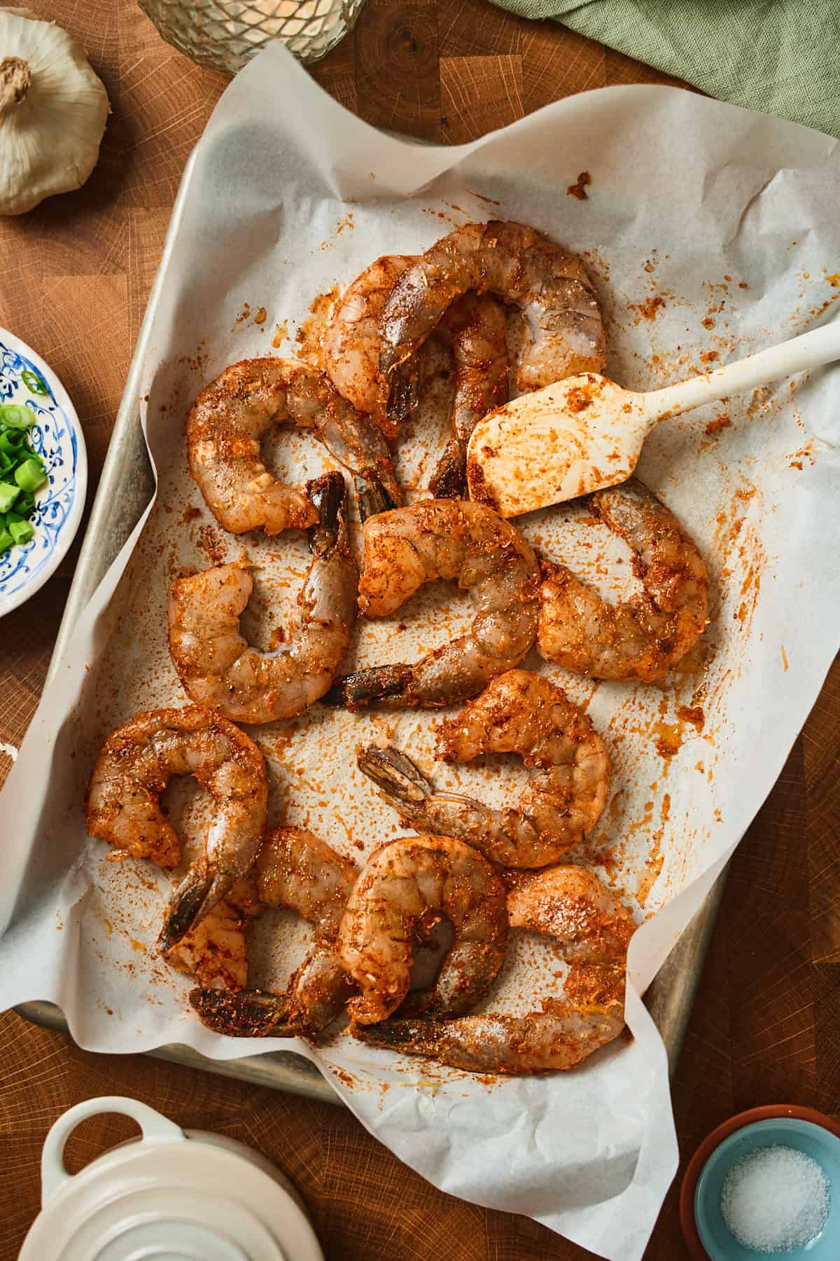 Raw colossal shrimp tossed with Cajun seasoning and lemon zest in a parchment-lined sheet pan.