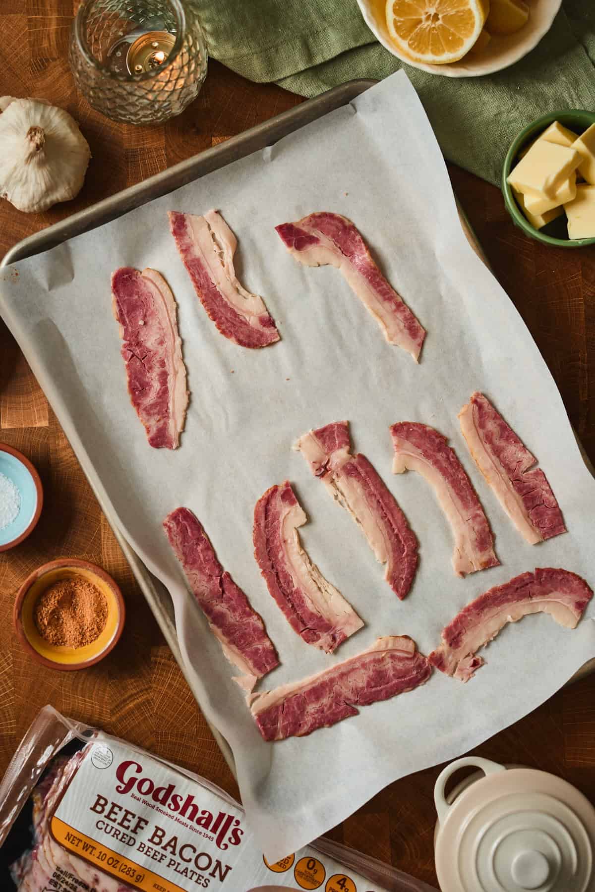 Quartered beef bacon arranged on a parchment-lined baking sheet, ready to go into the oven.