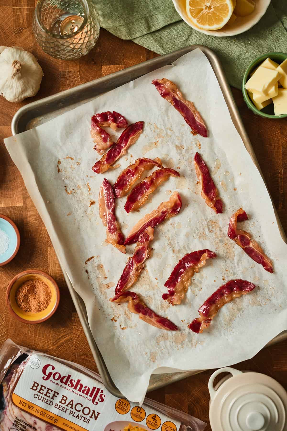 Quartered beef bacon arranged on a parchment-lined baking sheet, ready to par-render.