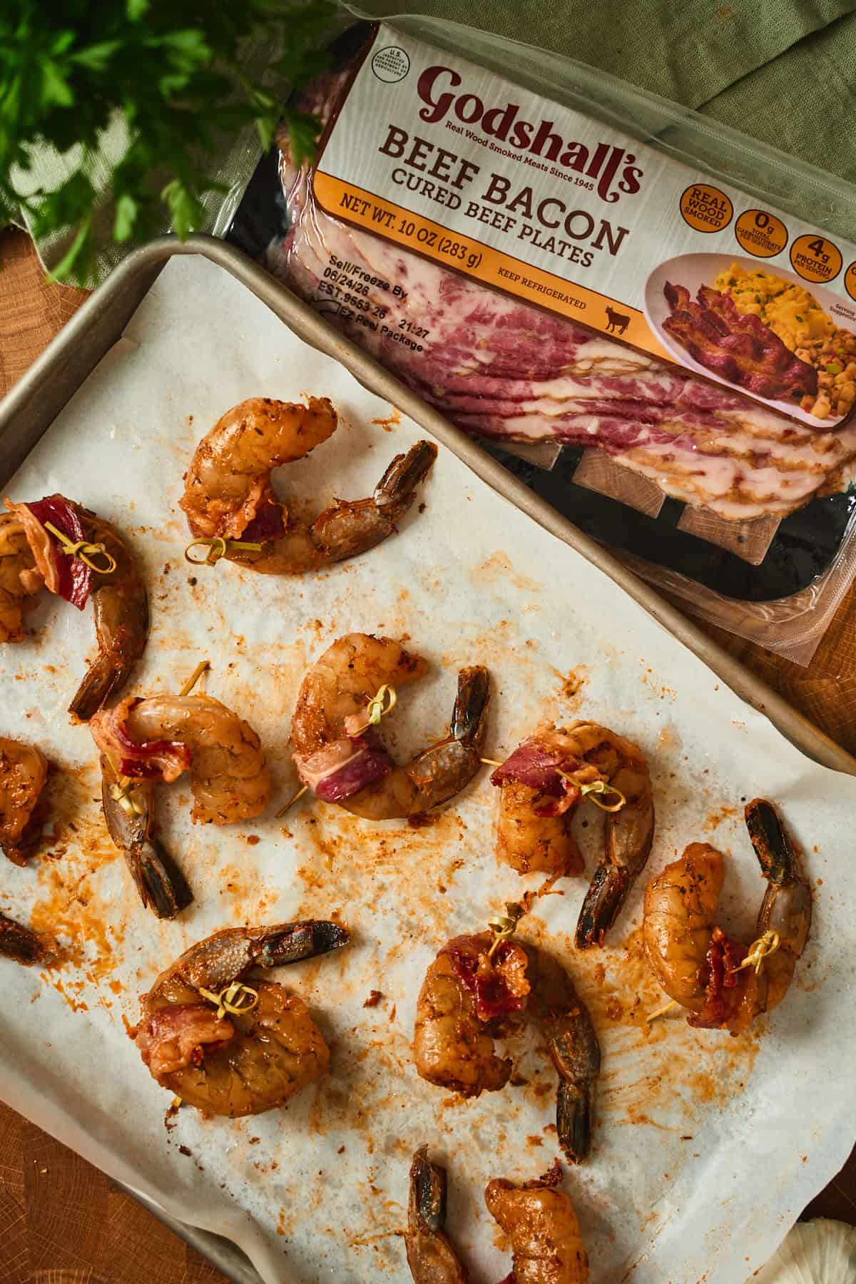 Cajun beef bacon wrapped shrimp secured with bamboo cocktail picks on a parchment-lined sheet pan.