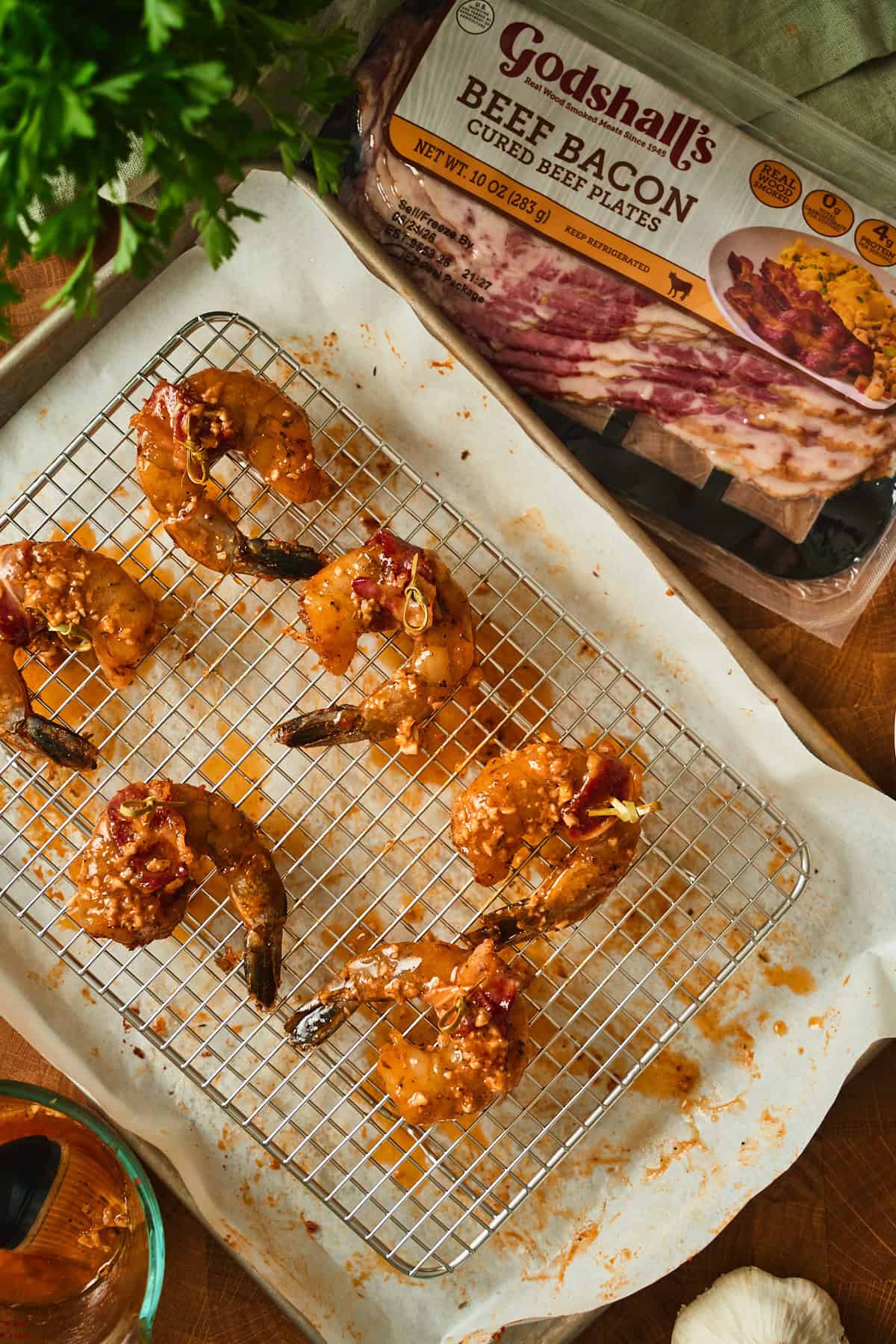 Cajun garlic lemon butter brushed over bacon wrapped shrimp on a wire rack set over a baking sheet.