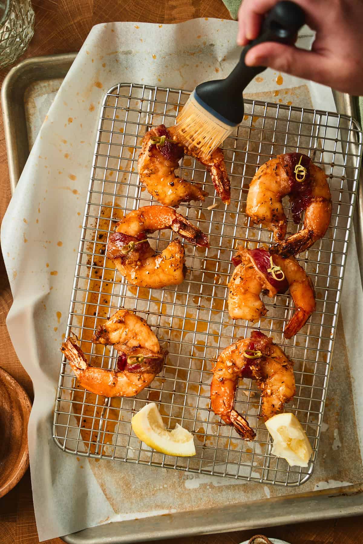 Hand brushing bacon wrapped shrimp with Cajun butter and adding fresh lemon to the shrimp.