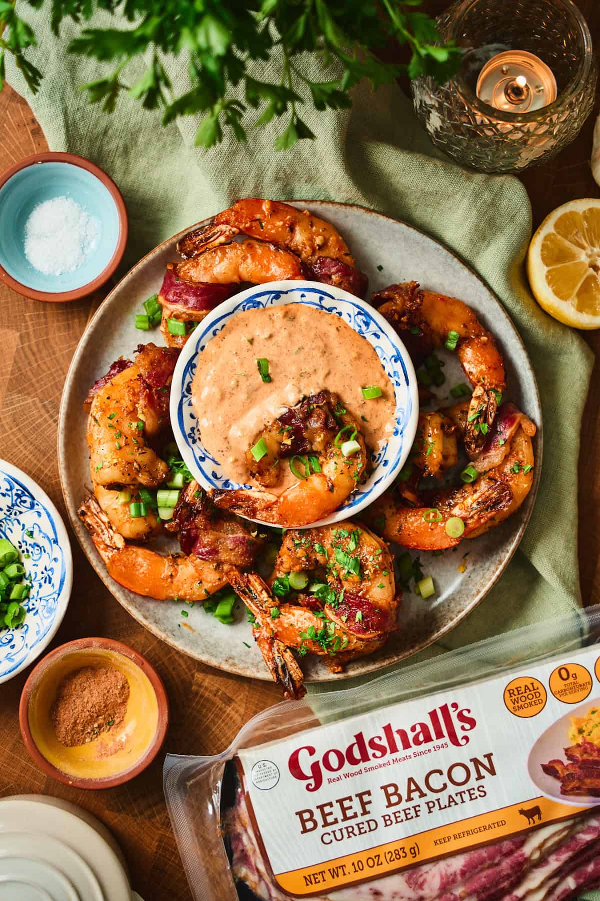 Overhead of Cajun bacon wrapped shrimp around a center bowl of remoulade with a package of Godshall's beef bacon alongside.