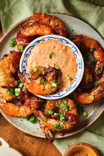 Cajun beef bacon wrapped shrimp on a plate with a bowl of remoulade.