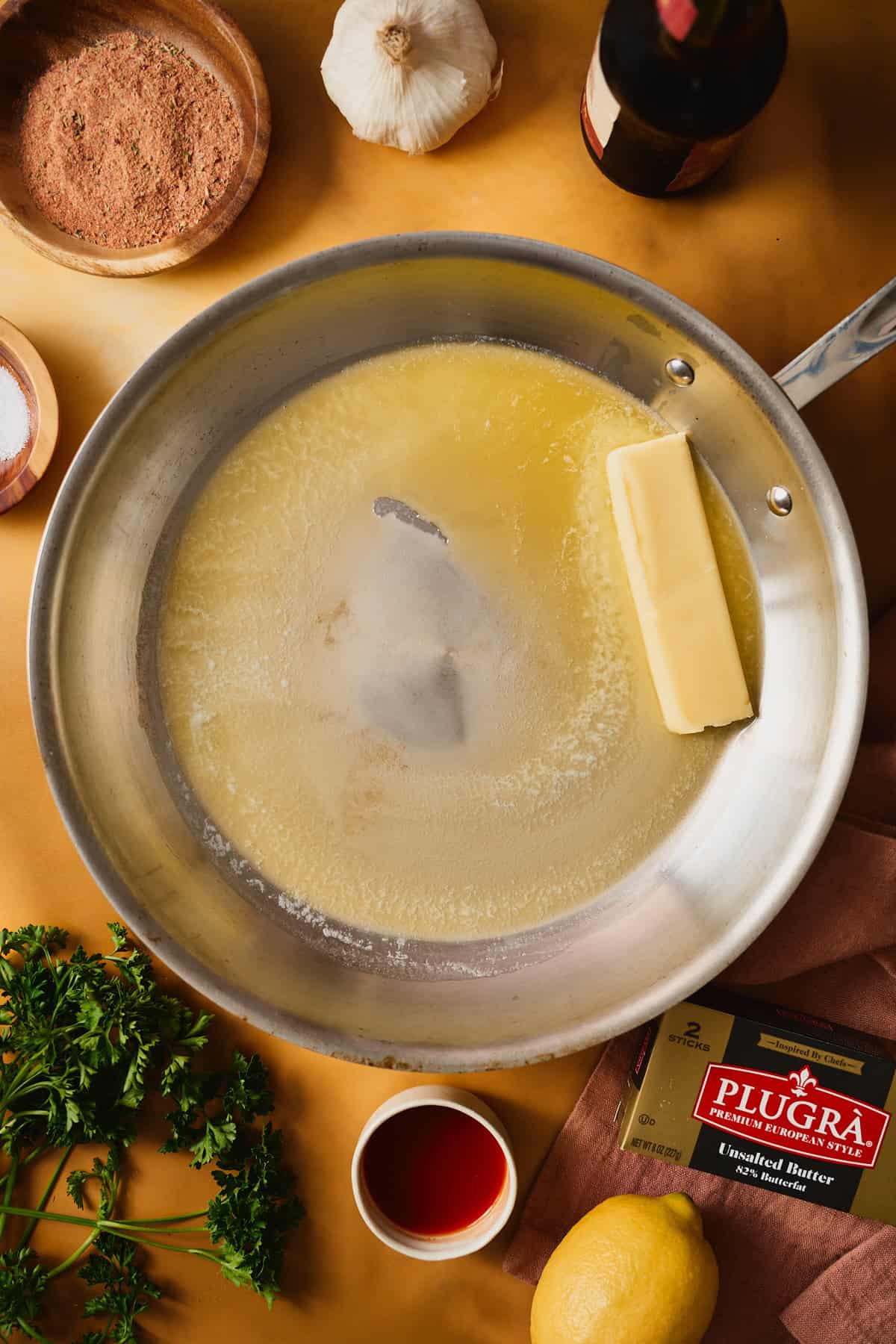A stick of Plugrà butter melting in a skillet alongside already-melted golden butter, the start of the garlic butter sauce.