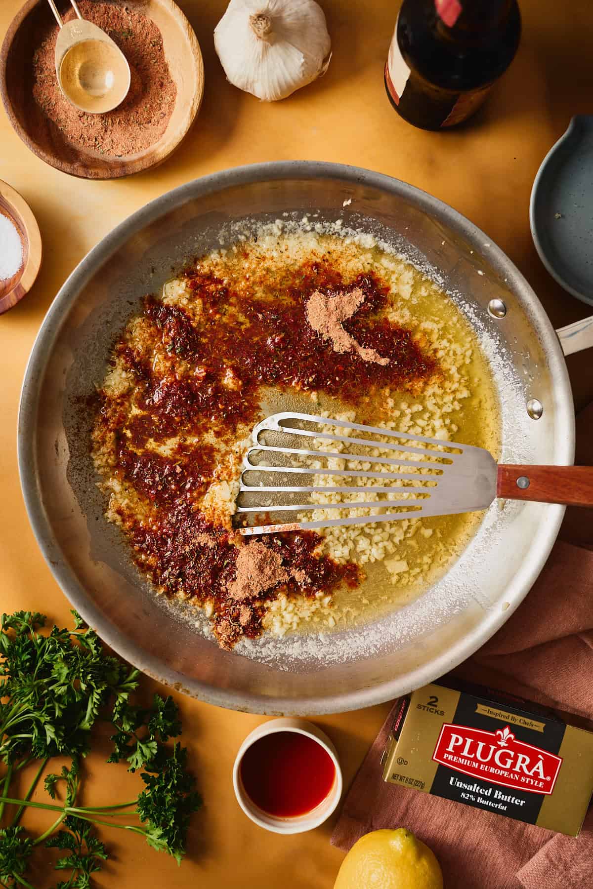 Garlic and seasoning blooming in melted butter in a skillet, deepening to a rich red-brown, a fish spatula stirring it through.