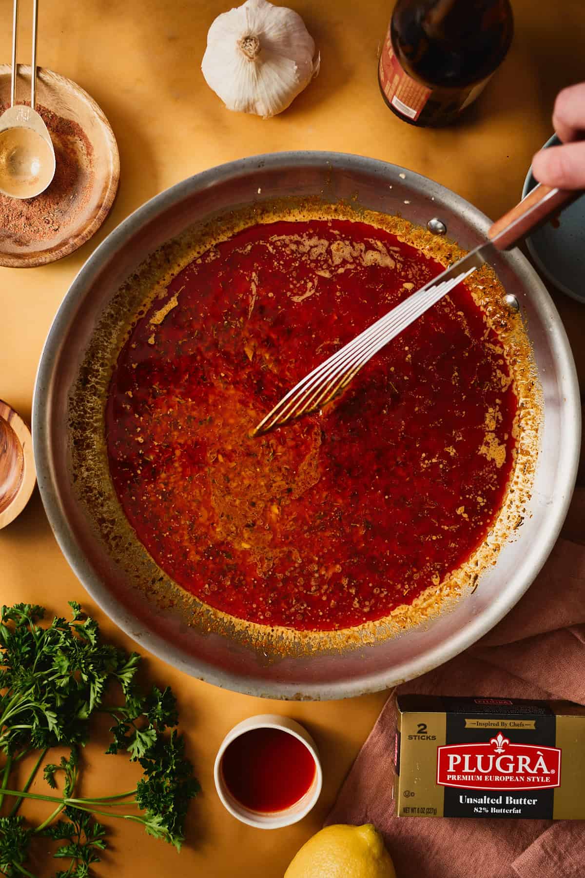 A spatula stirring simmering Cajun garlic butter sauce in a skillet, the surface bubbling and turning glossy red-orange.