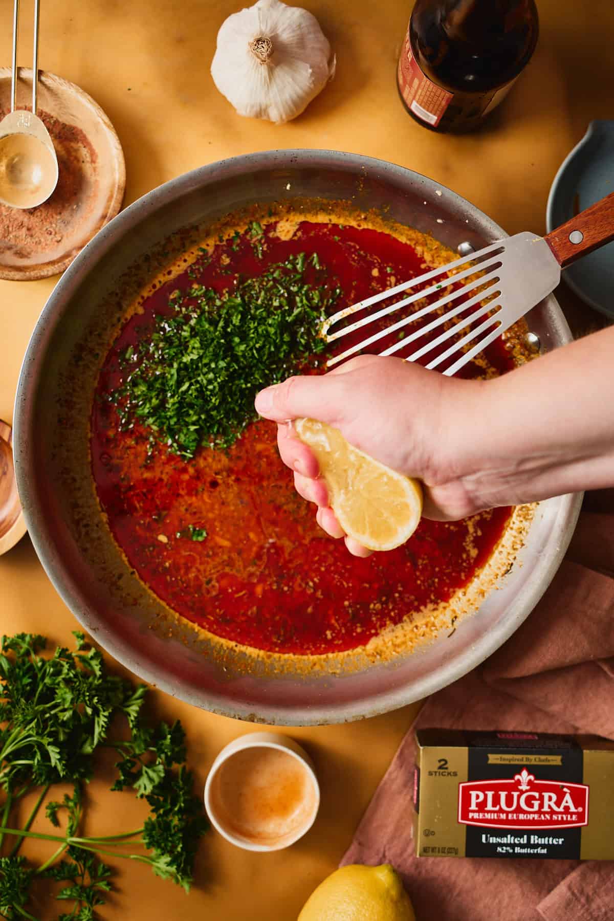 Hand squeezing a lemon overtop of a skillet with Cajun butter sauce and fresh parsley.