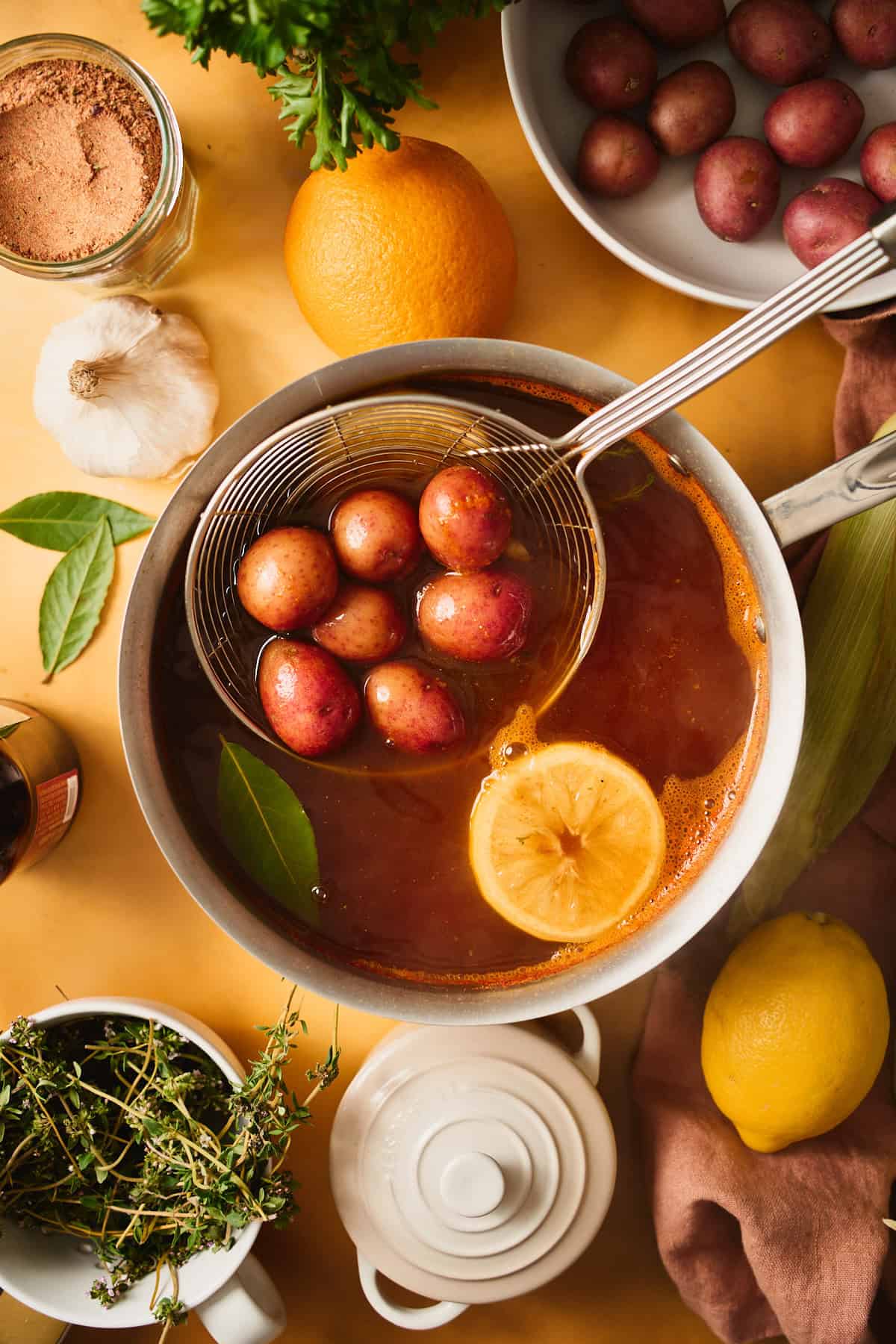 Adding small potatoes to a pot of boiling, seasoned water on a yellow backdrop.