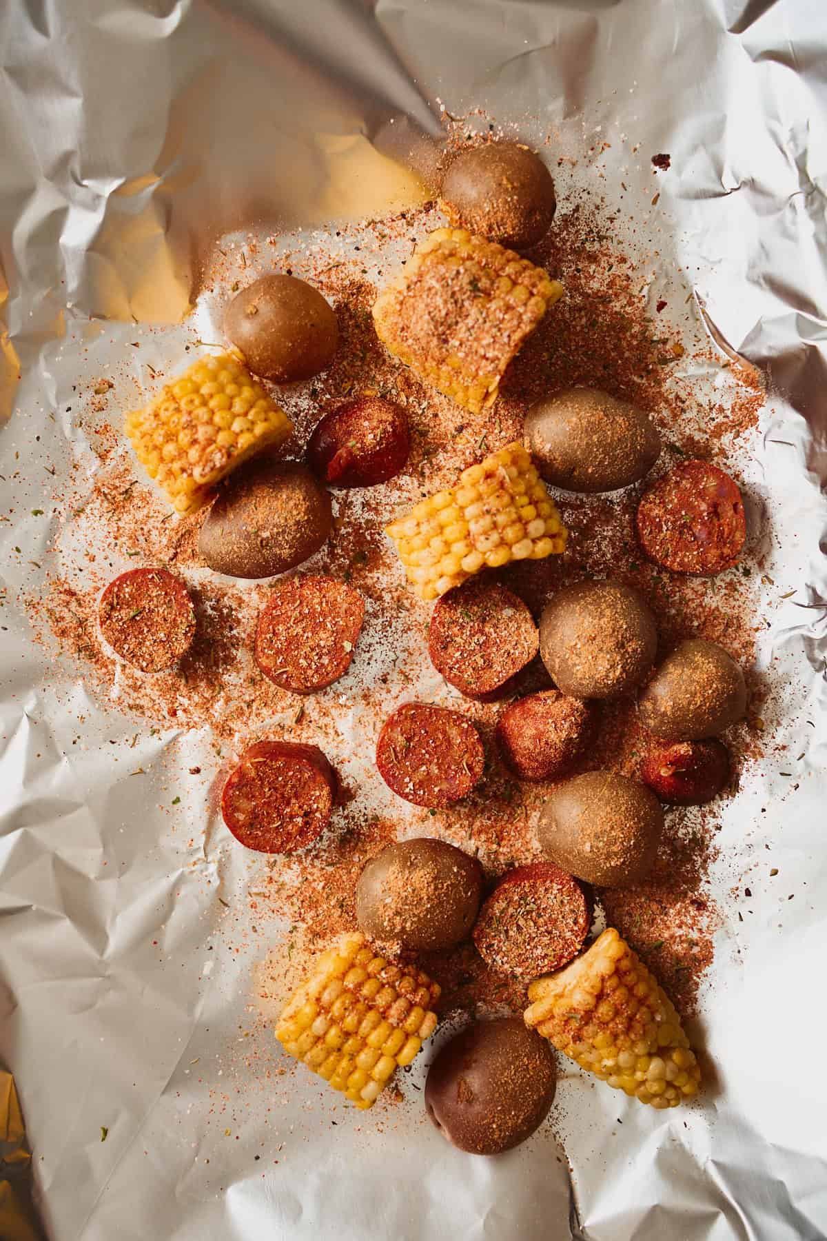 Par-boiled baby potatoes, sliced andouille, and corn cobbettes arranged on a sheet of foil and dusted with Cajun seasoning before saucing.