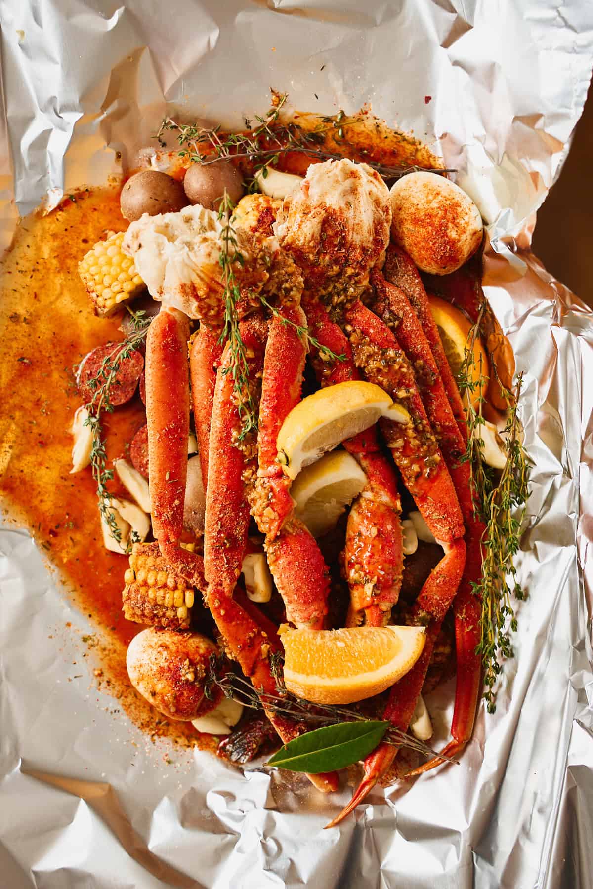 Snow crab clusters layered on top of a foil packet with potatoes, corn, lemon and orange wedges, thyme, and a bay leaf.