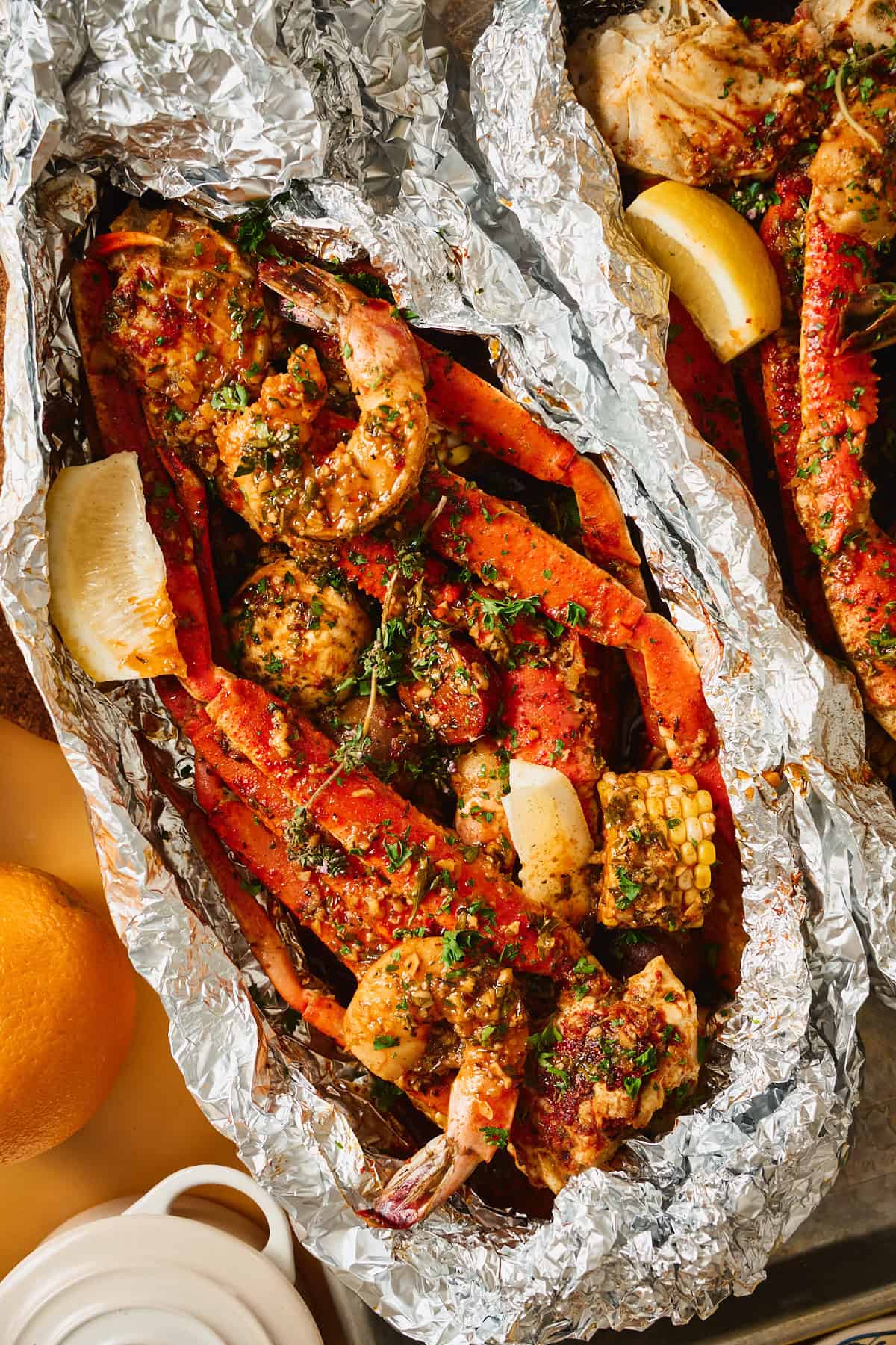 Close-up of an open foil packet of Cajun seafood boil with butter-glazed snow crab legs, shrimp, corn, and potatoes in garlic butter sauce.
