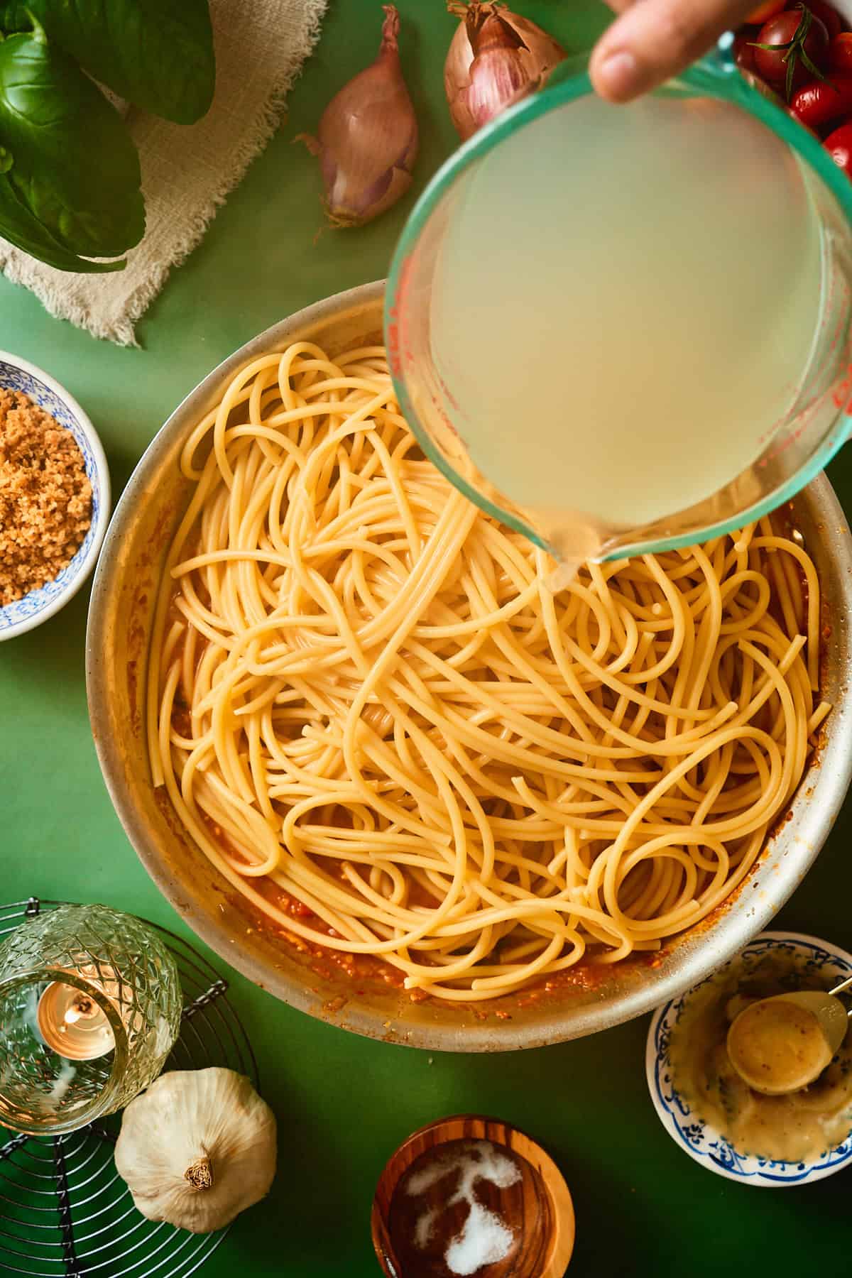 Starchy pasta water poured over bucatini and tomato sauce to make a glossy bacon tomato pasta.