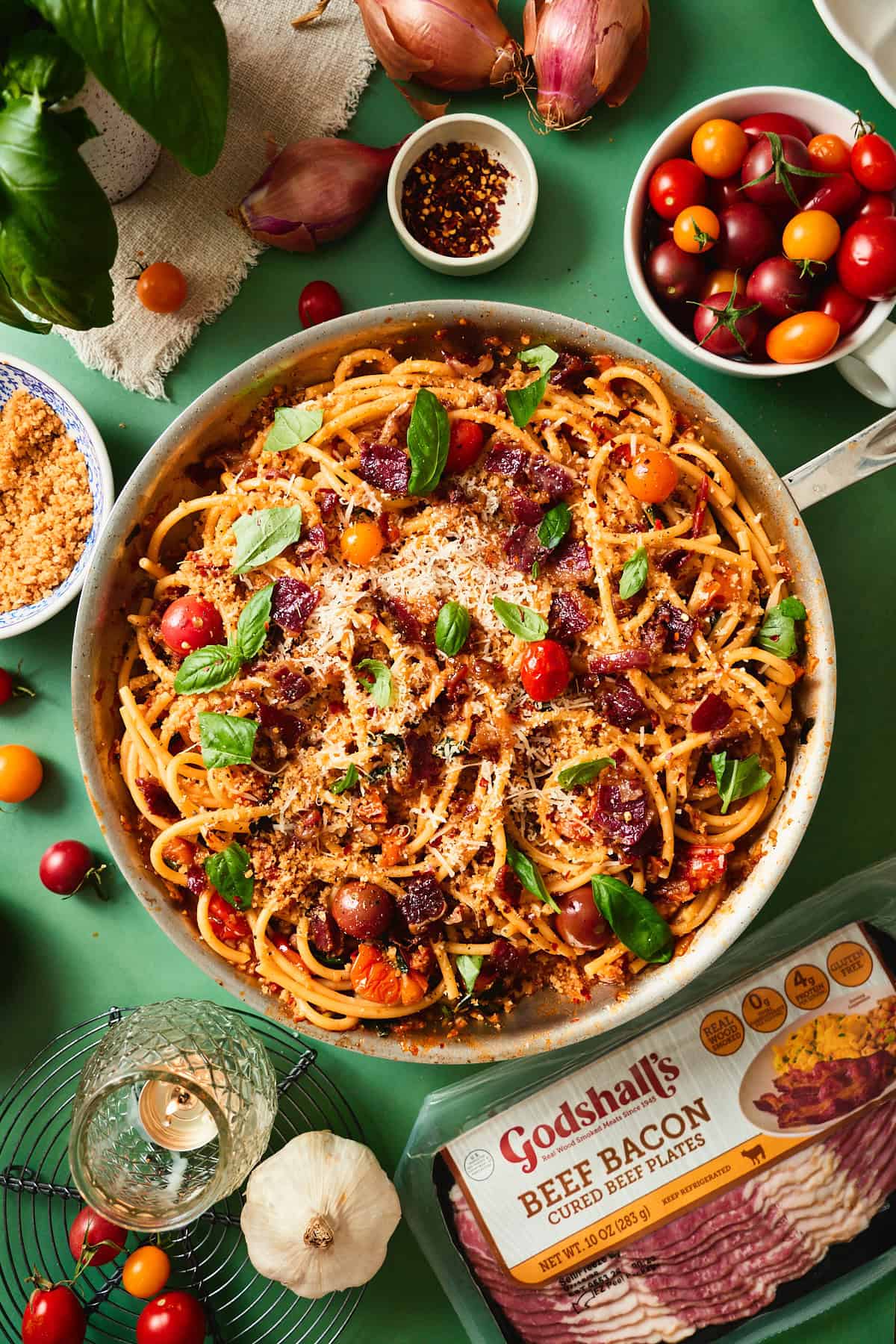Bacon tomato pasta in a wood bowl next to a package of Godshall's beef bacon, with cherry tomatoes and Parmesan.