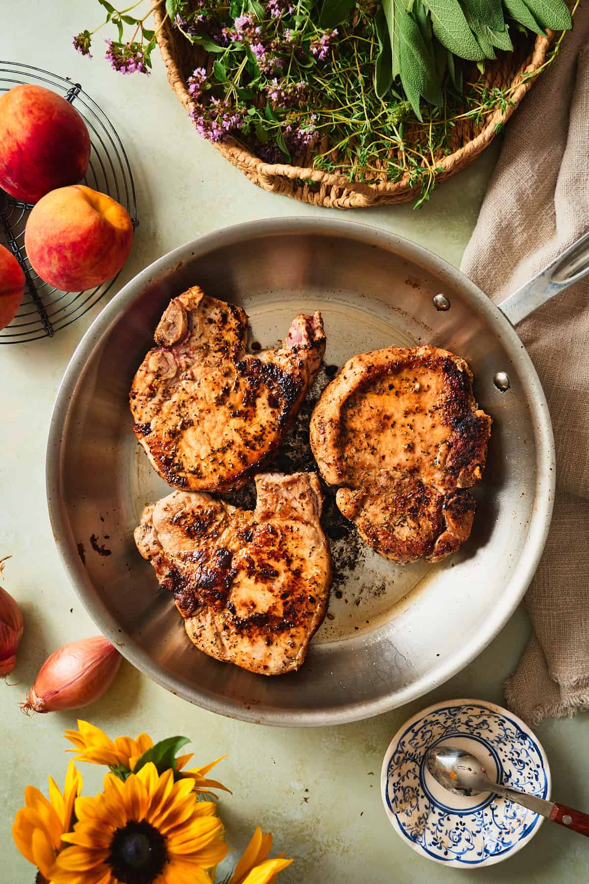 Bone-in pork chops searing to a golden crust in a stainless skillet.
