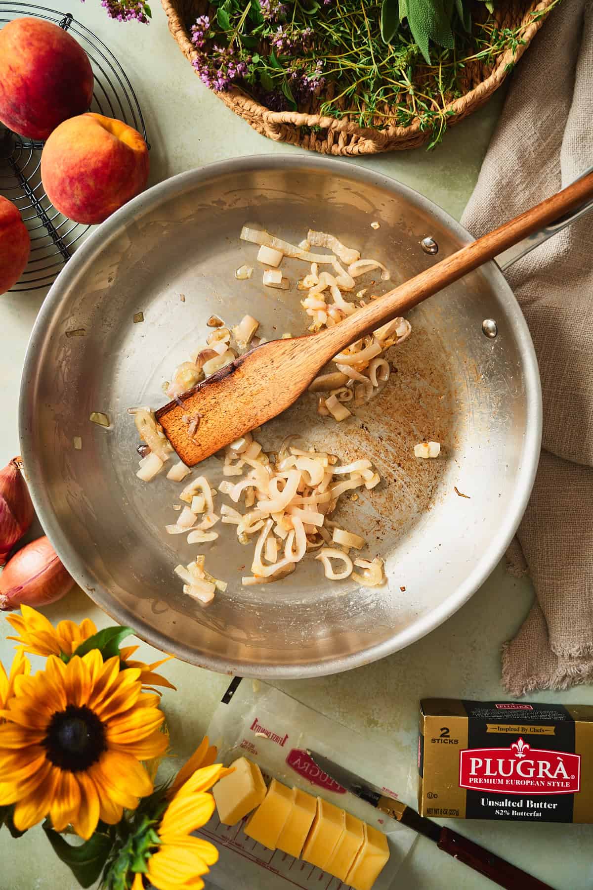 Sliced shallots softening in butter in a stainless skillet with cubed Plugrà alongside.