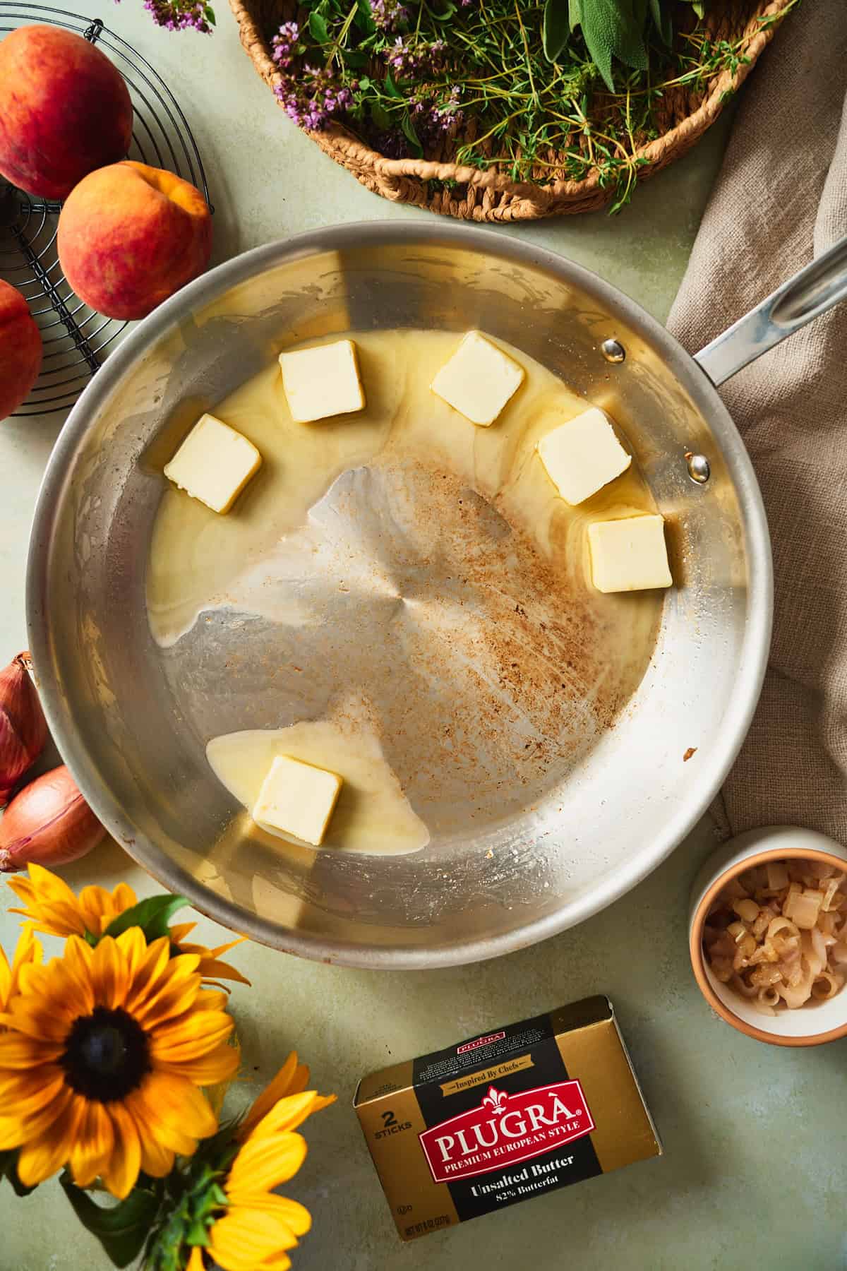 Cubes of Plugrà melting in a stainless skillet, cooked shallots waiting in a bowl.