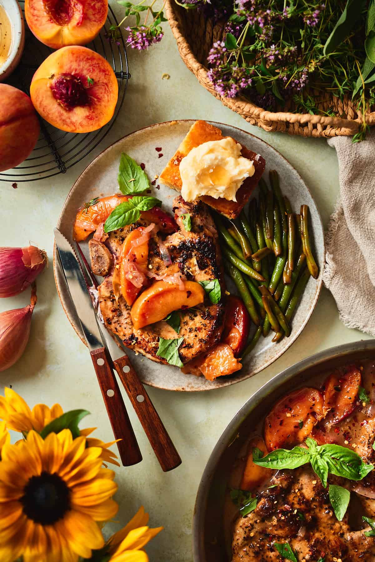 Bone-in peach pork chop with pan sauce, served with green beans and cornbread under melting honey butter.
