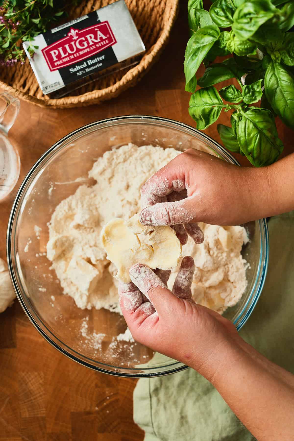 Hands flattening a cube of butter into a sheet between fingers to make a flaky galette crust.