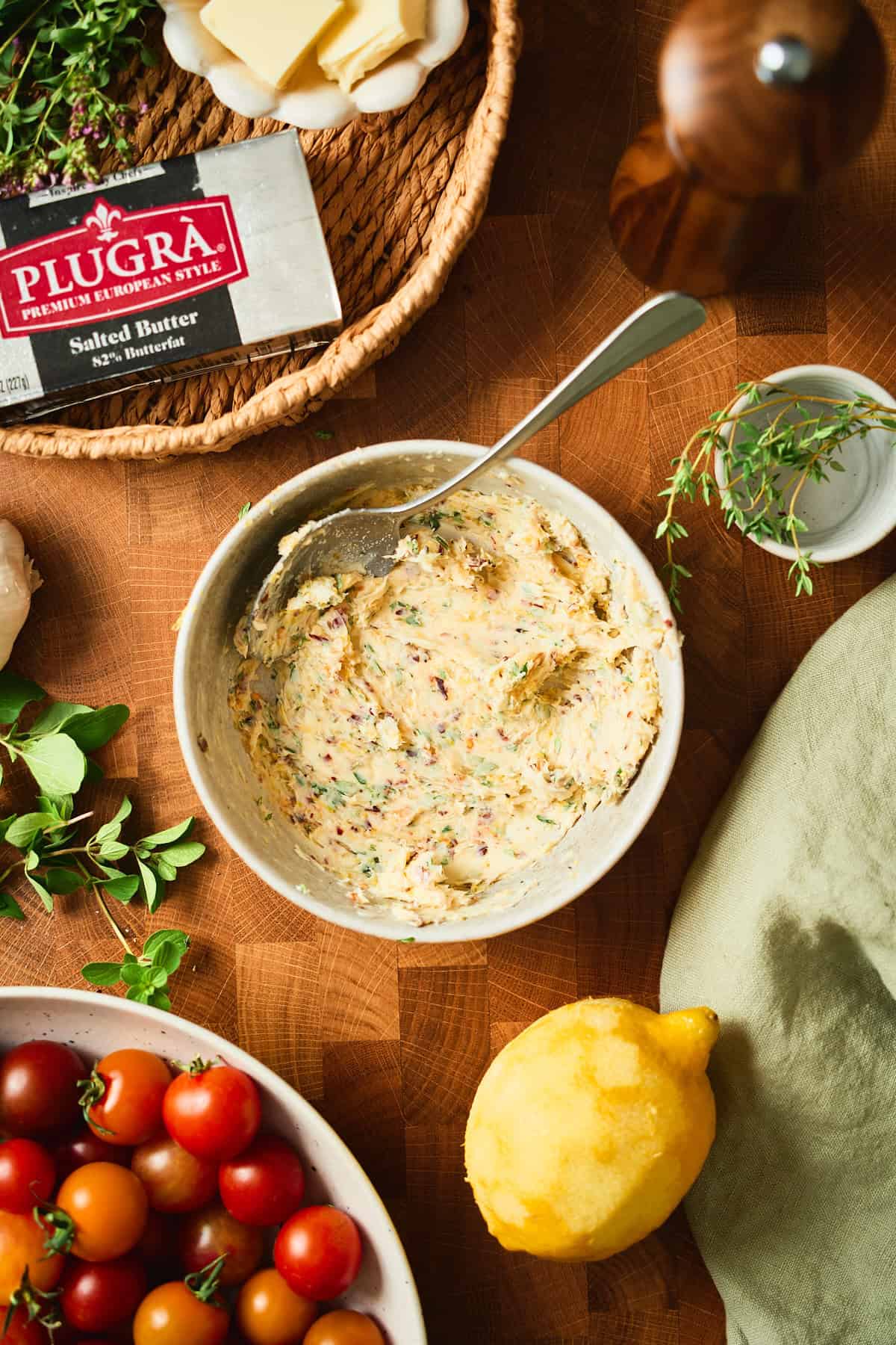 Garlic herb compound butter mixed in a bowl next to Plugrà salted butter, fresh herbs, and a lemon.