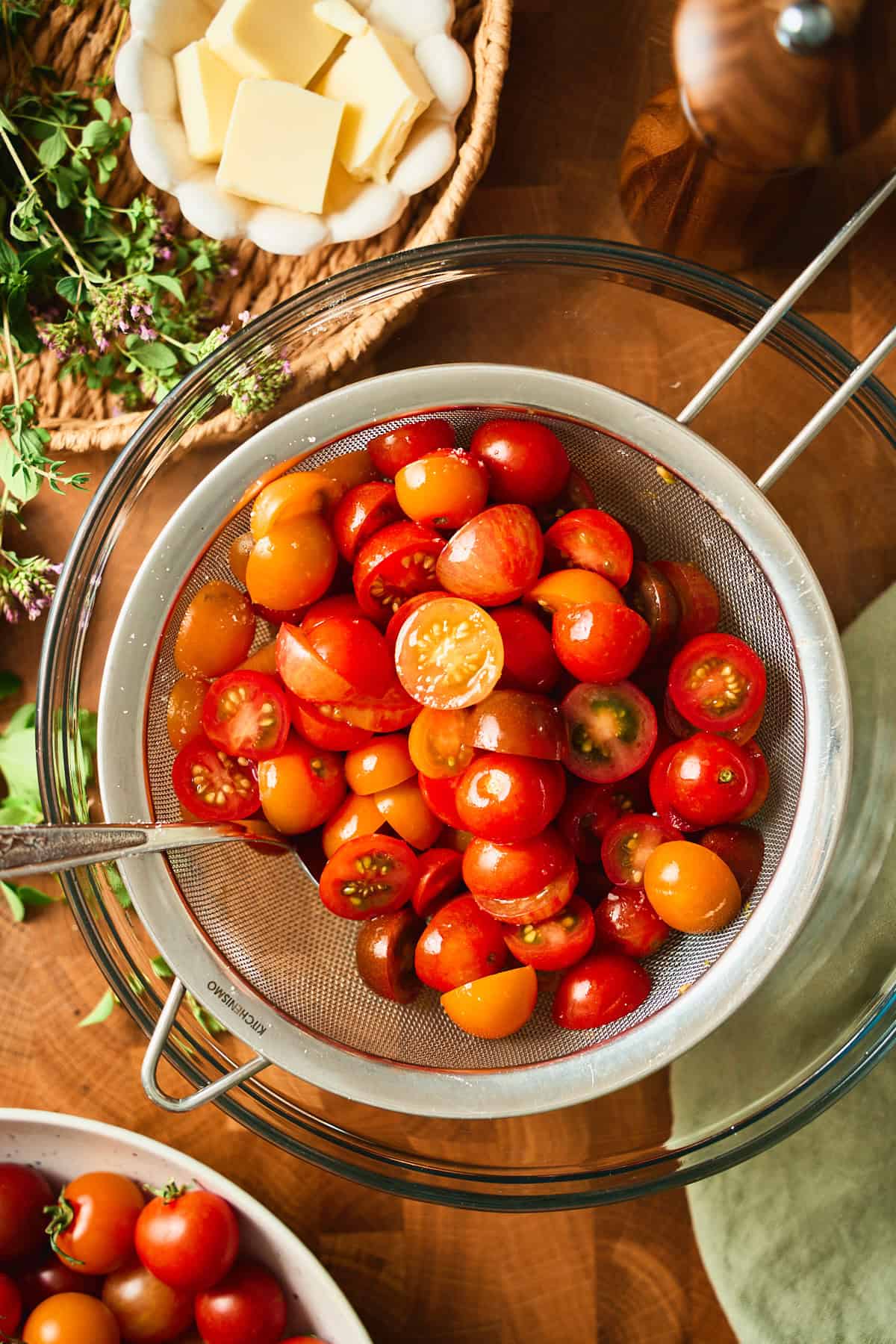 Halved cherry tomatoes salted and draining in a fine mesh sieve set over a glass bowl.