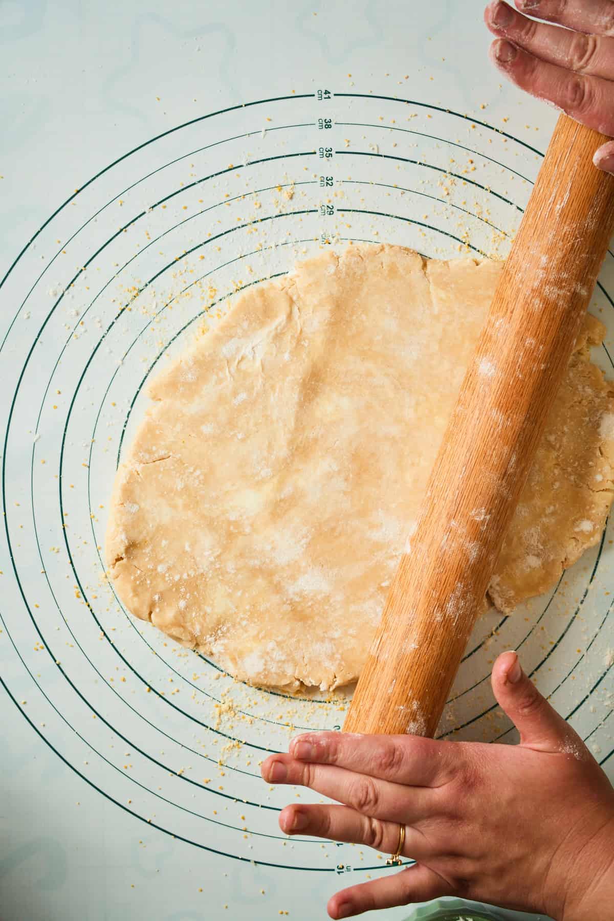 Hands rolling chilled galette dough with a wooden rolling pin.
