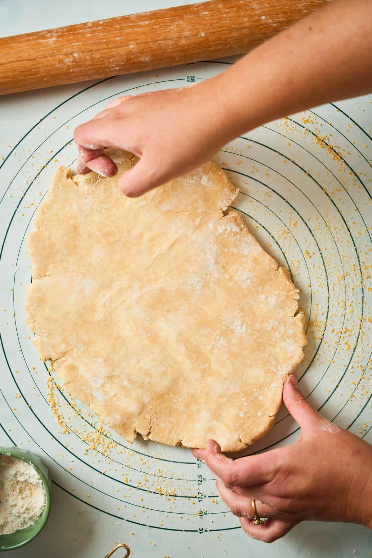 Hands pressing cracks along the edge of a rolled galette dough round back together.