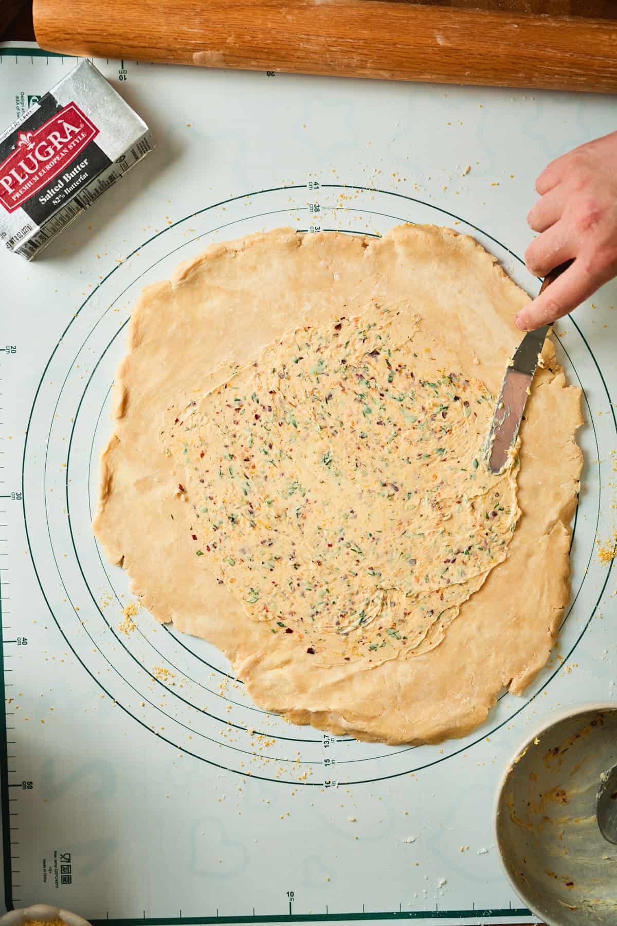 Garlic herb butter spread over a galette dough round with an offset spatula, leaving a clean border.