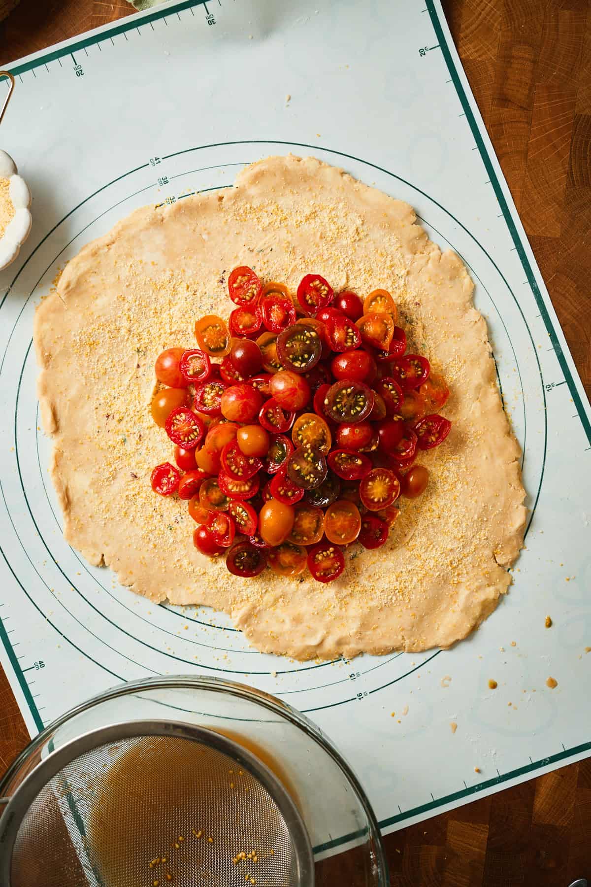Halved cherry tomatoes packed cut side up in the center of galette dough over cornmeal and herb butter.