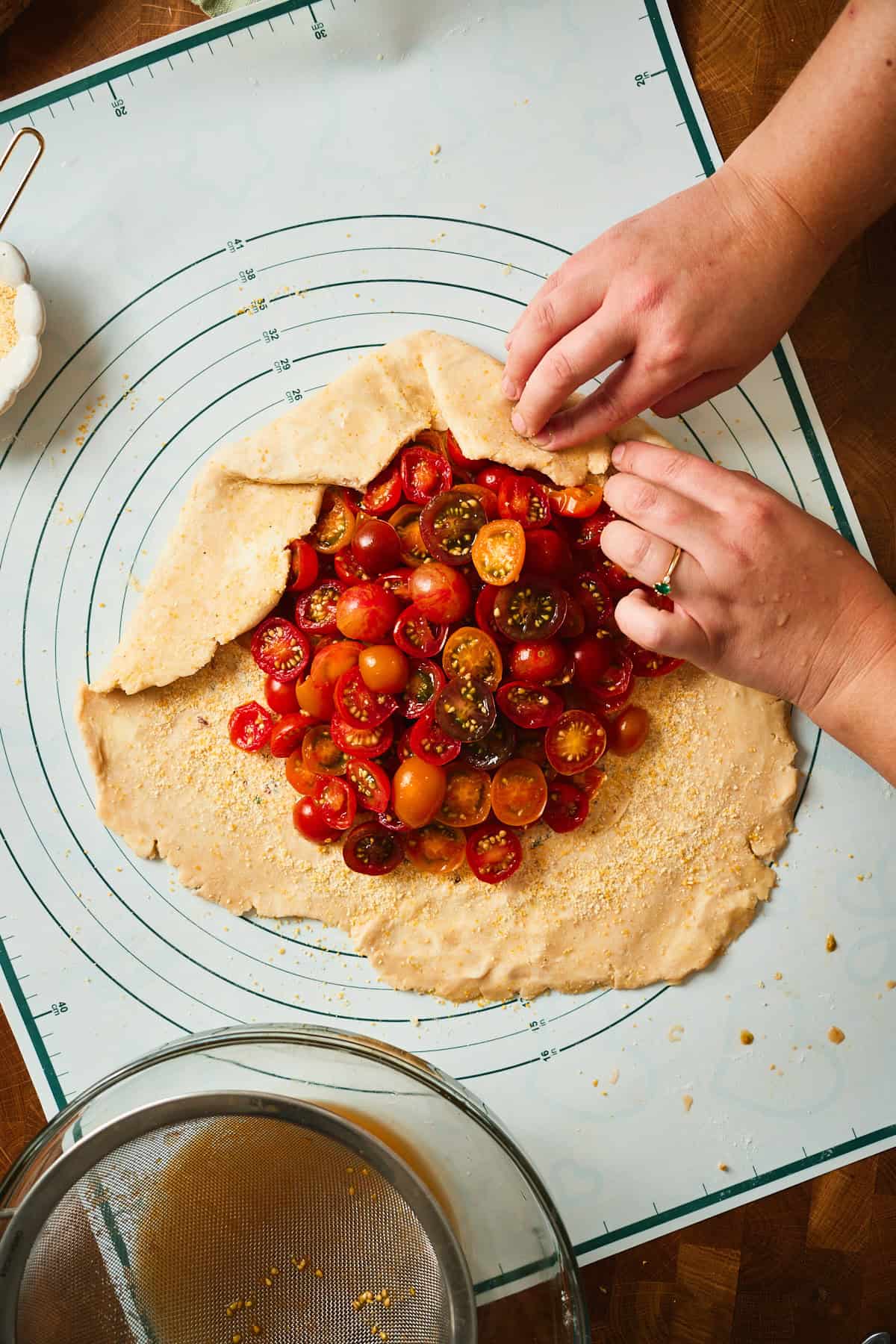 Hands folding and pleating the border of a tomato galette up over the filling.