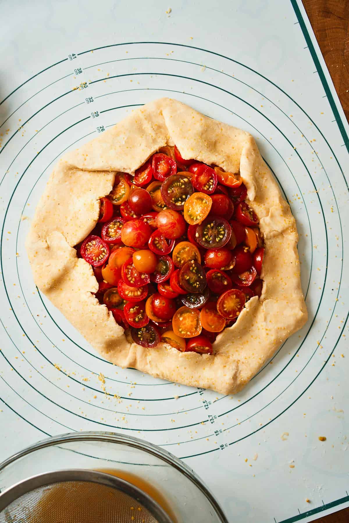 Assembled unbaked tomato galette on a parchment-lined sheet pan, dusted with cornmeal.
