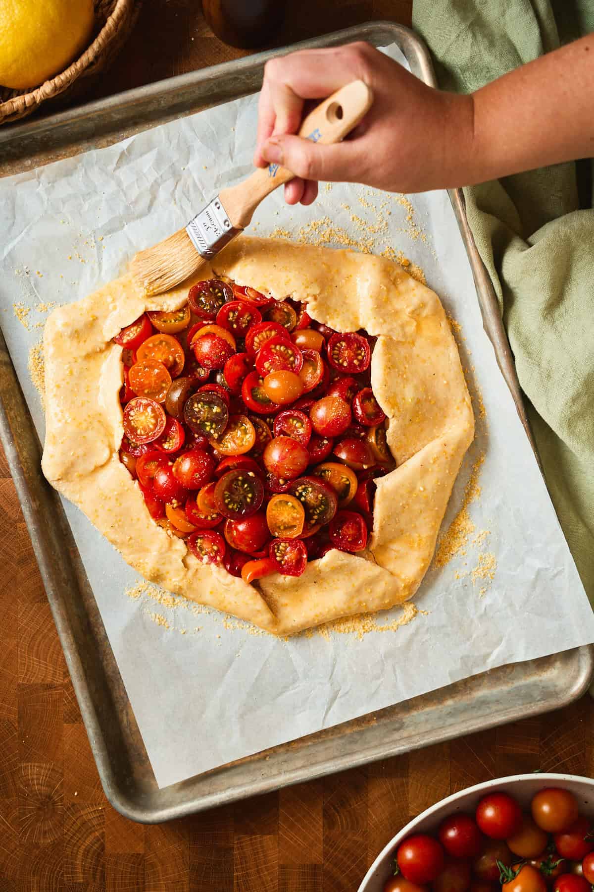 Egg wash brushed over the pleated crust of an unbaked tomato galette on a sheet pan.