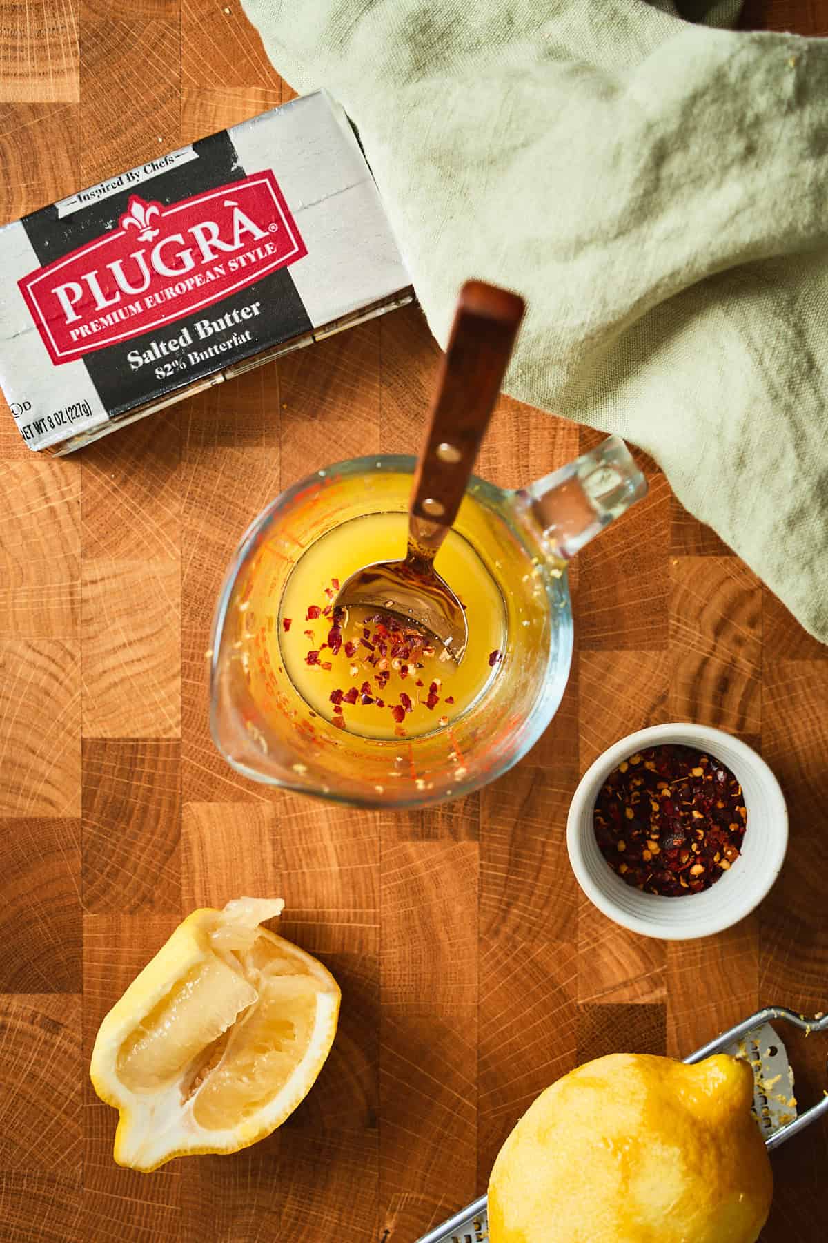 Melted Plugrà butter stirred with lemon juice, lemon zest, and red pepper flakes in a glass measuring cup.